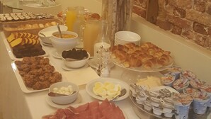 A buffet table with various food items, a vase with flowers, and a brick wall in the background. - Hotel Tiepolo (Venice)