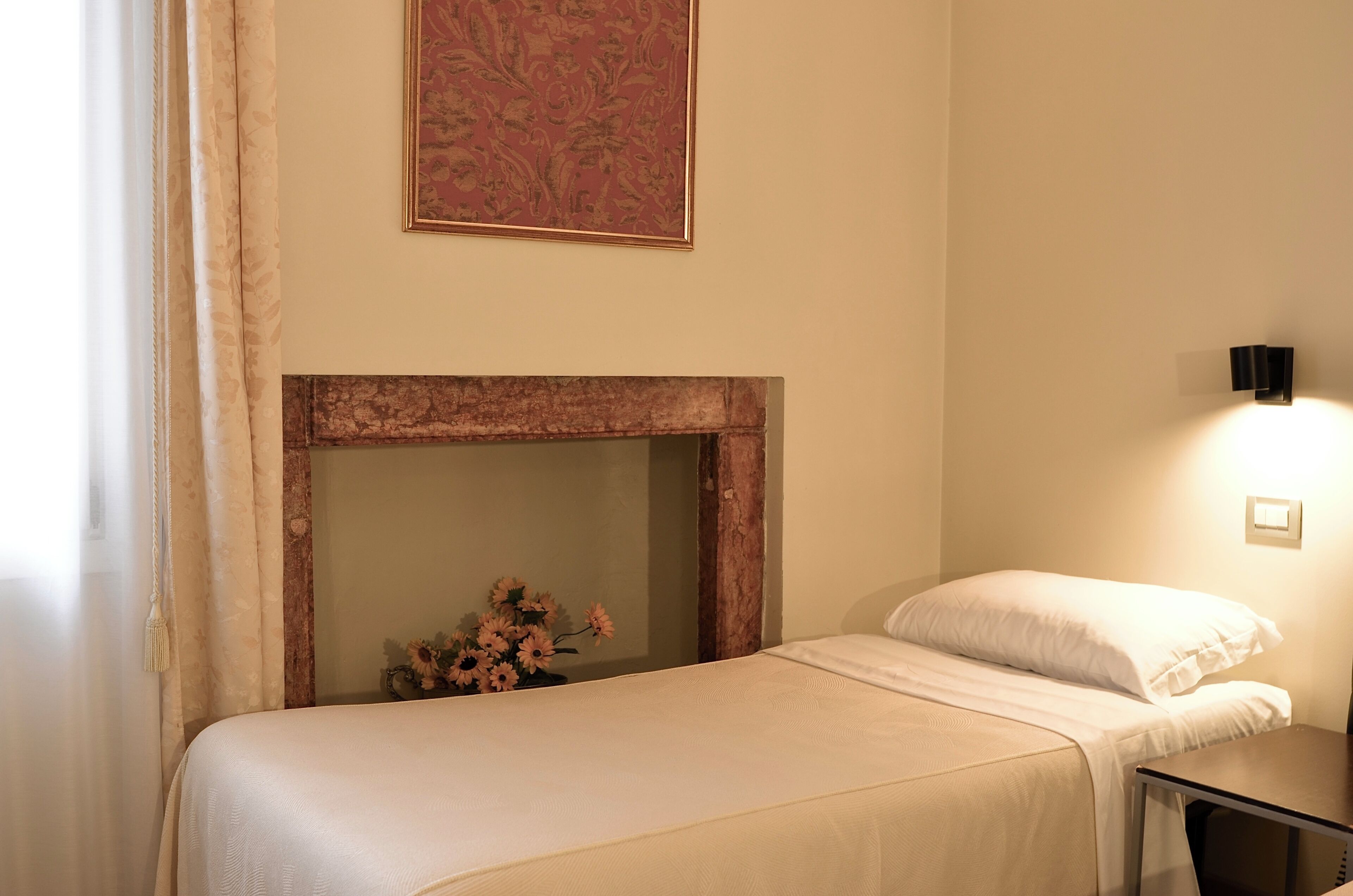 Habitación de hotel con cama, una mesita, luz en la pared, chimenea y una obra de arte enmarcada.