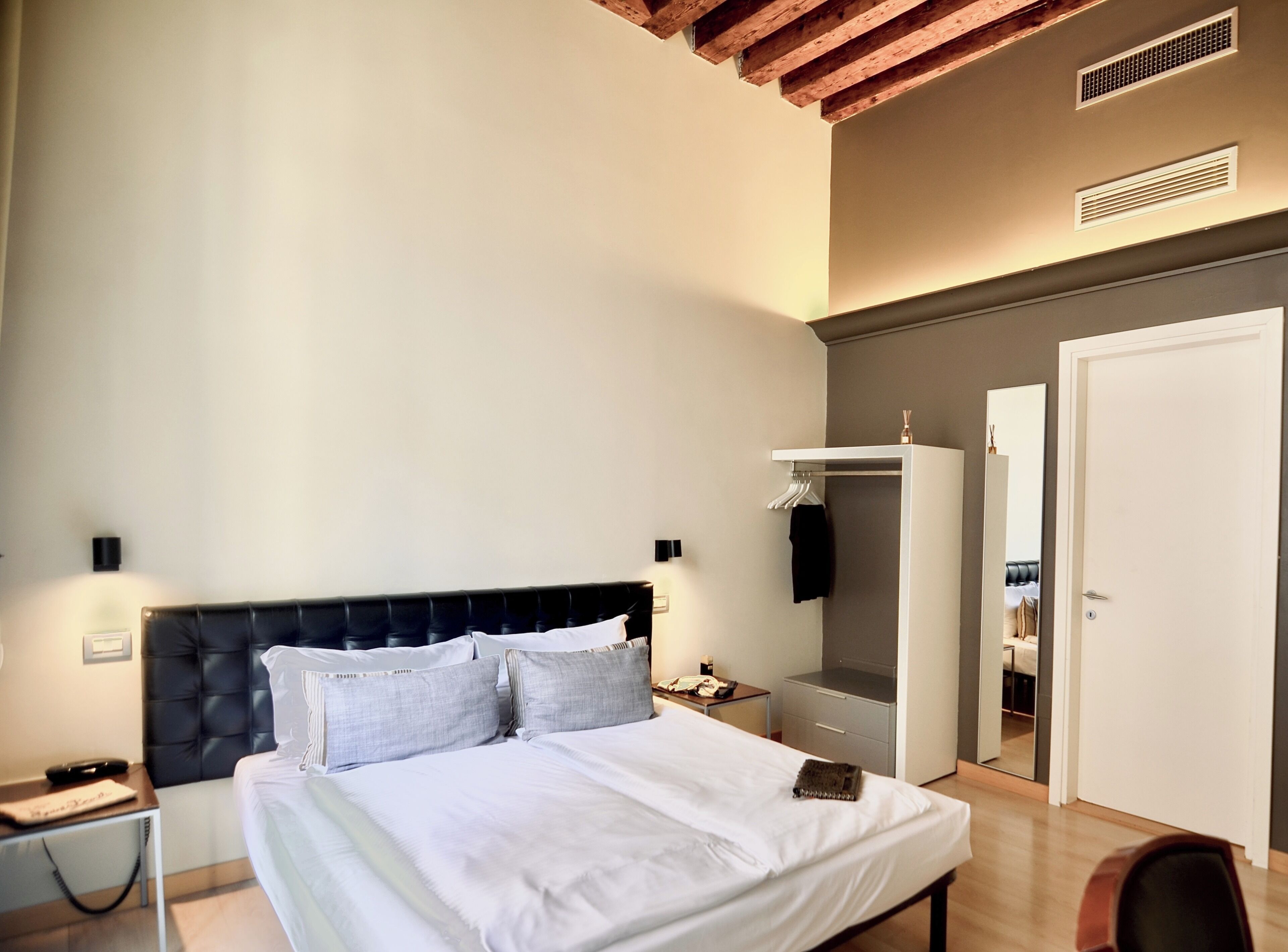 Une chambre à coucher comprenant un lit, une table de chevet, une commode, une armoire, un miroir et une porte.