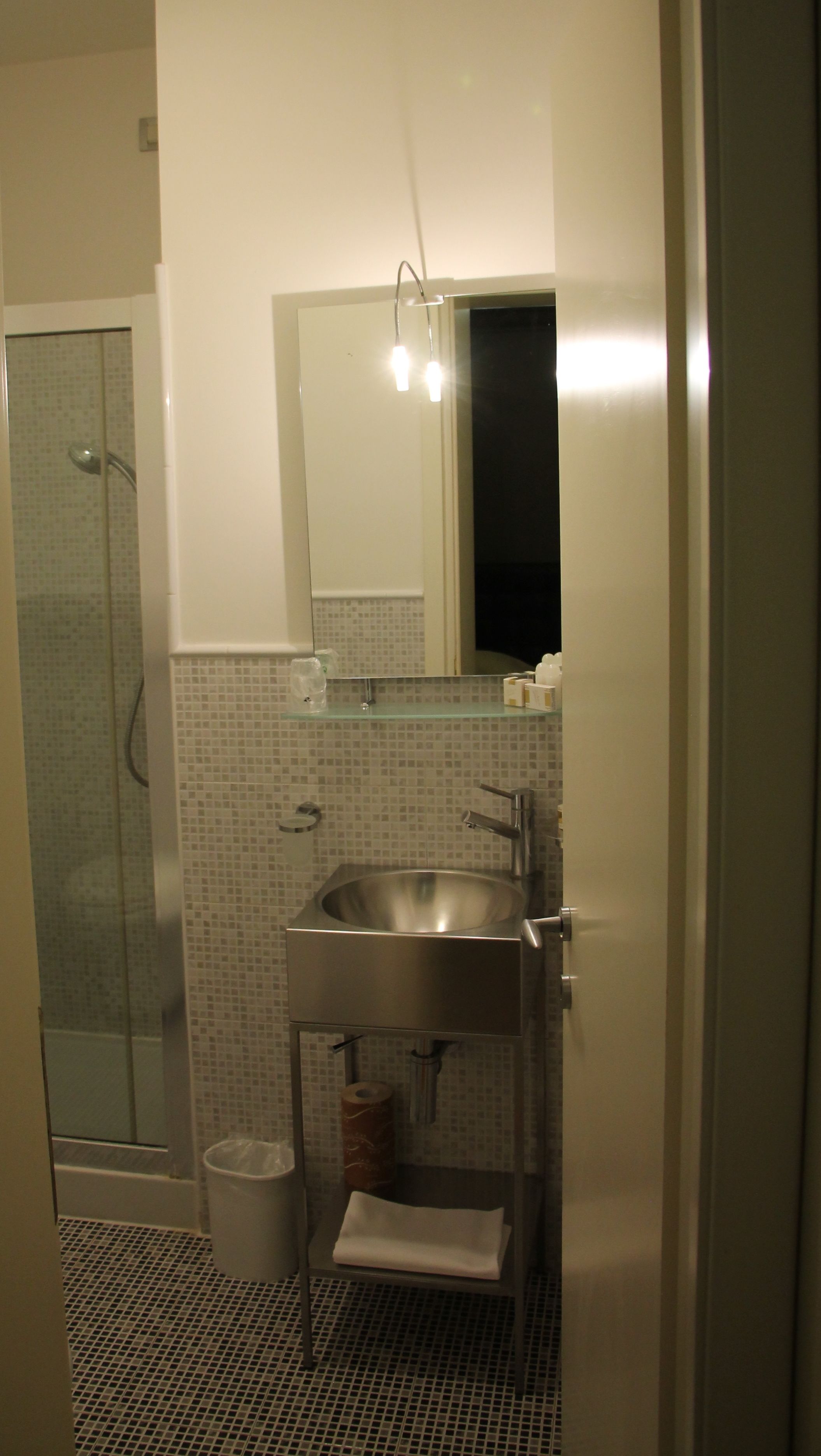 Un baño con cabina de ducha de vidrio, un lavamanos con espejo y suelo de baldosas.