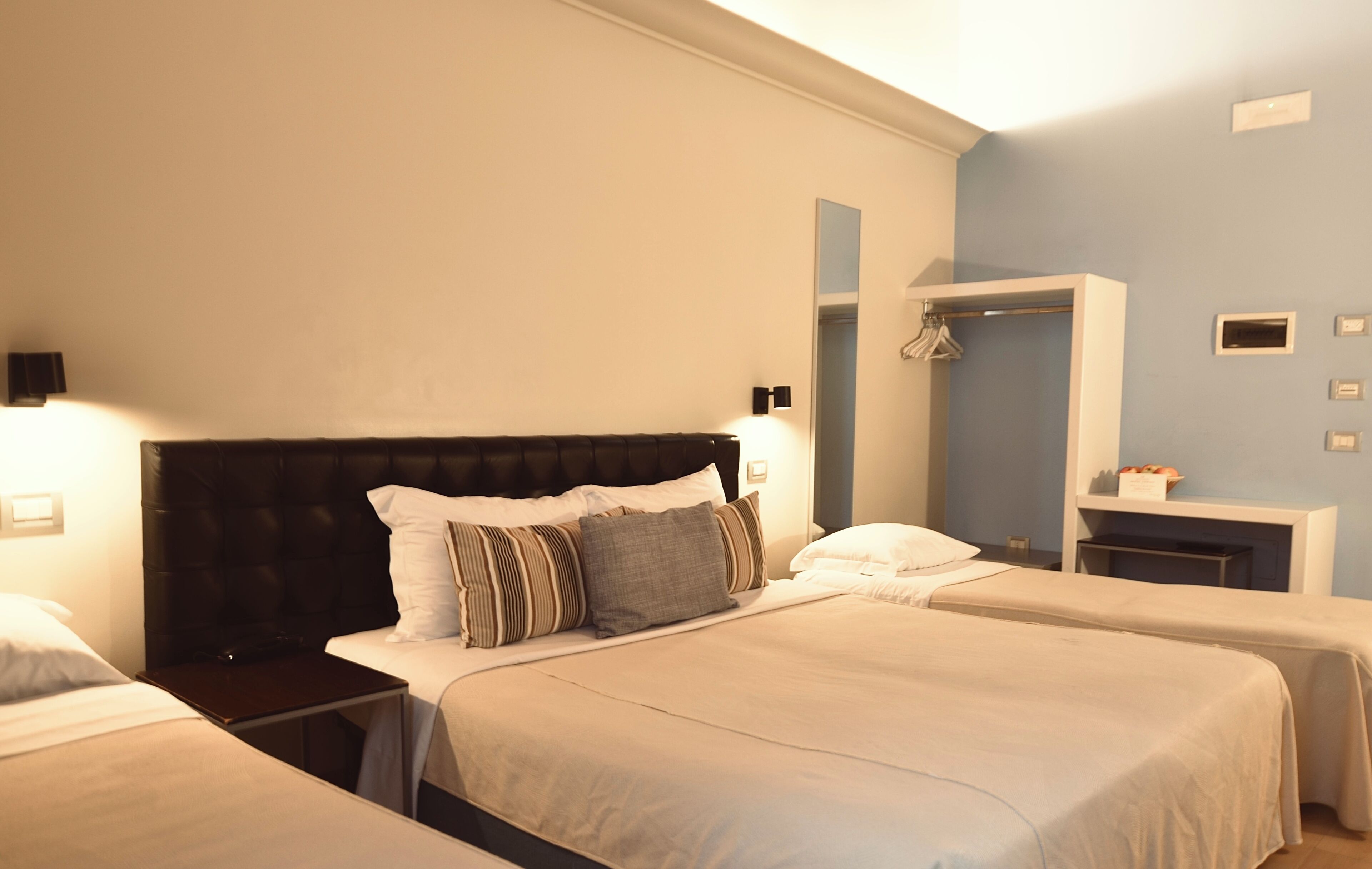 A hotel room with two beds, a dark headboard, bedside lamps, a mirror, a small table, and a wardrobe.
