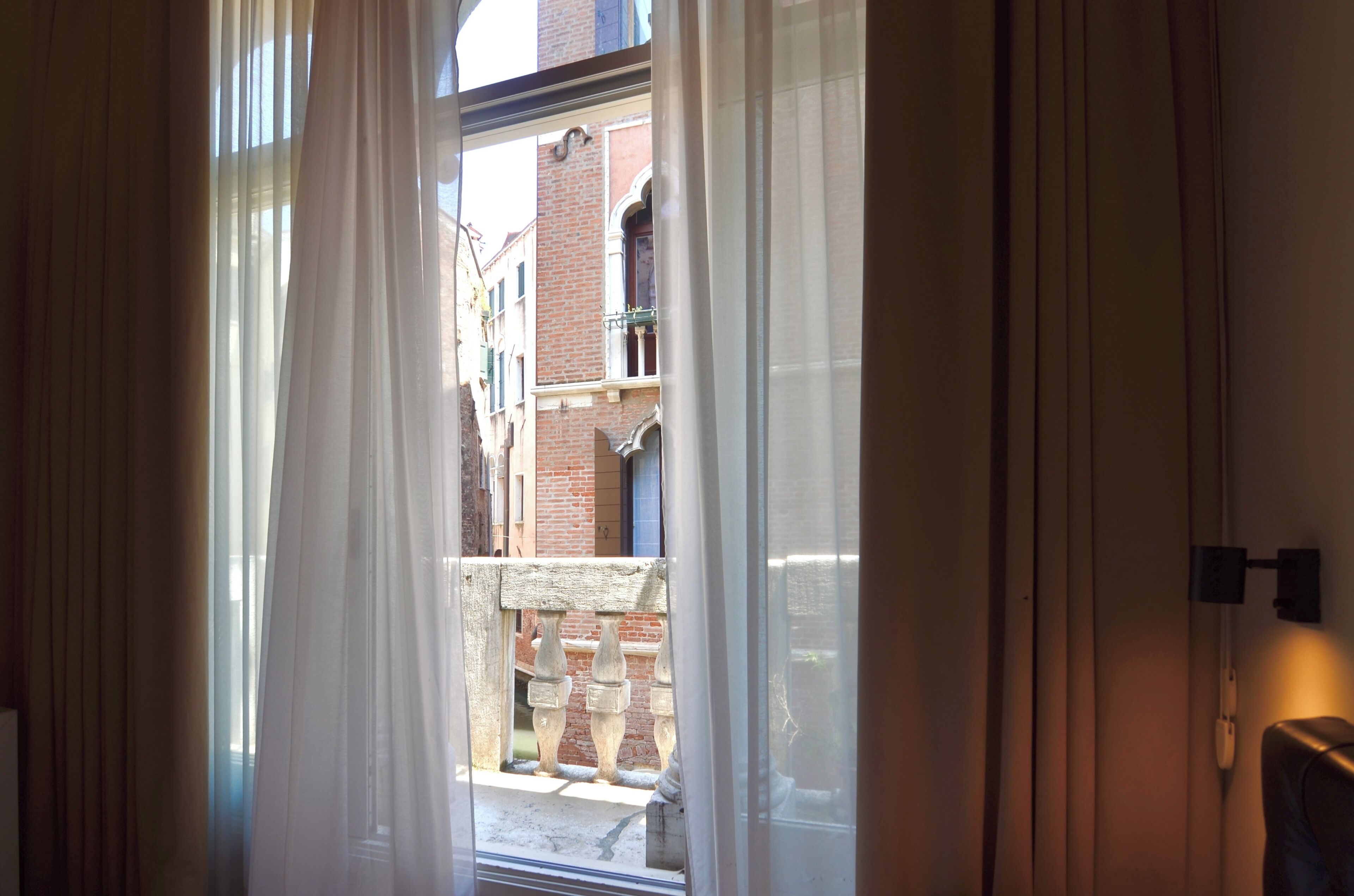 Una habitación con vista a un edificio de ladrillo a través de una ventana con cortinas translúcidas.