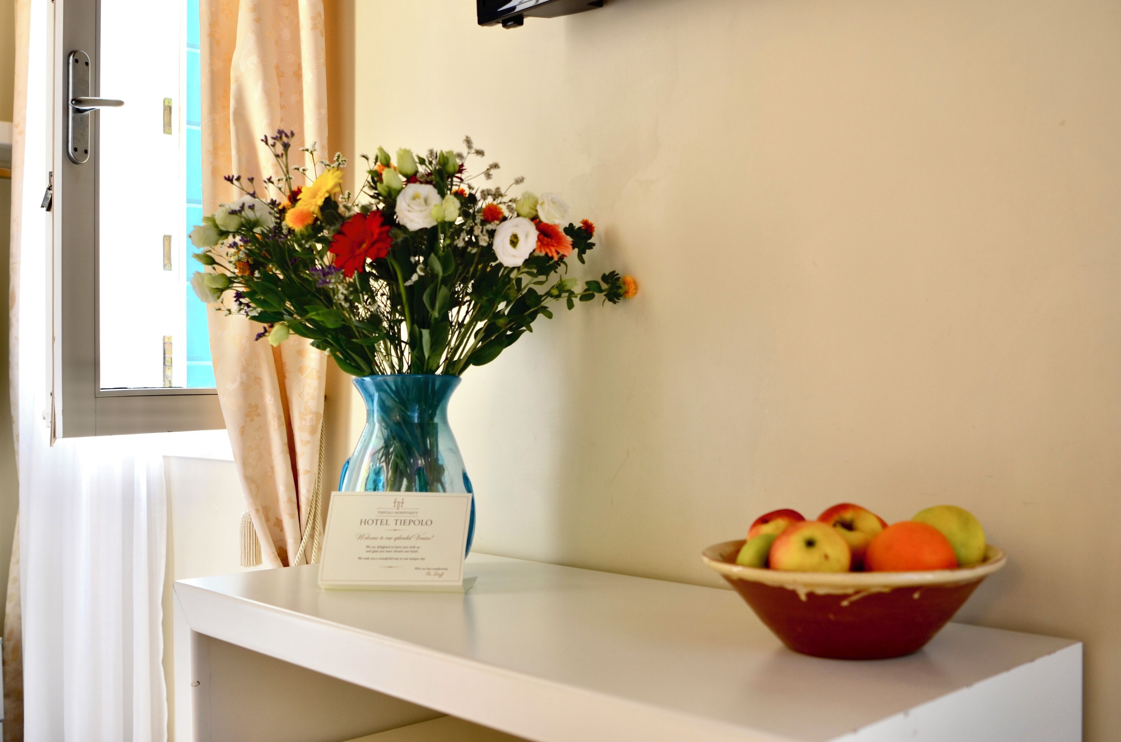 A white table with a vase of flowers and a bowl of fruit.