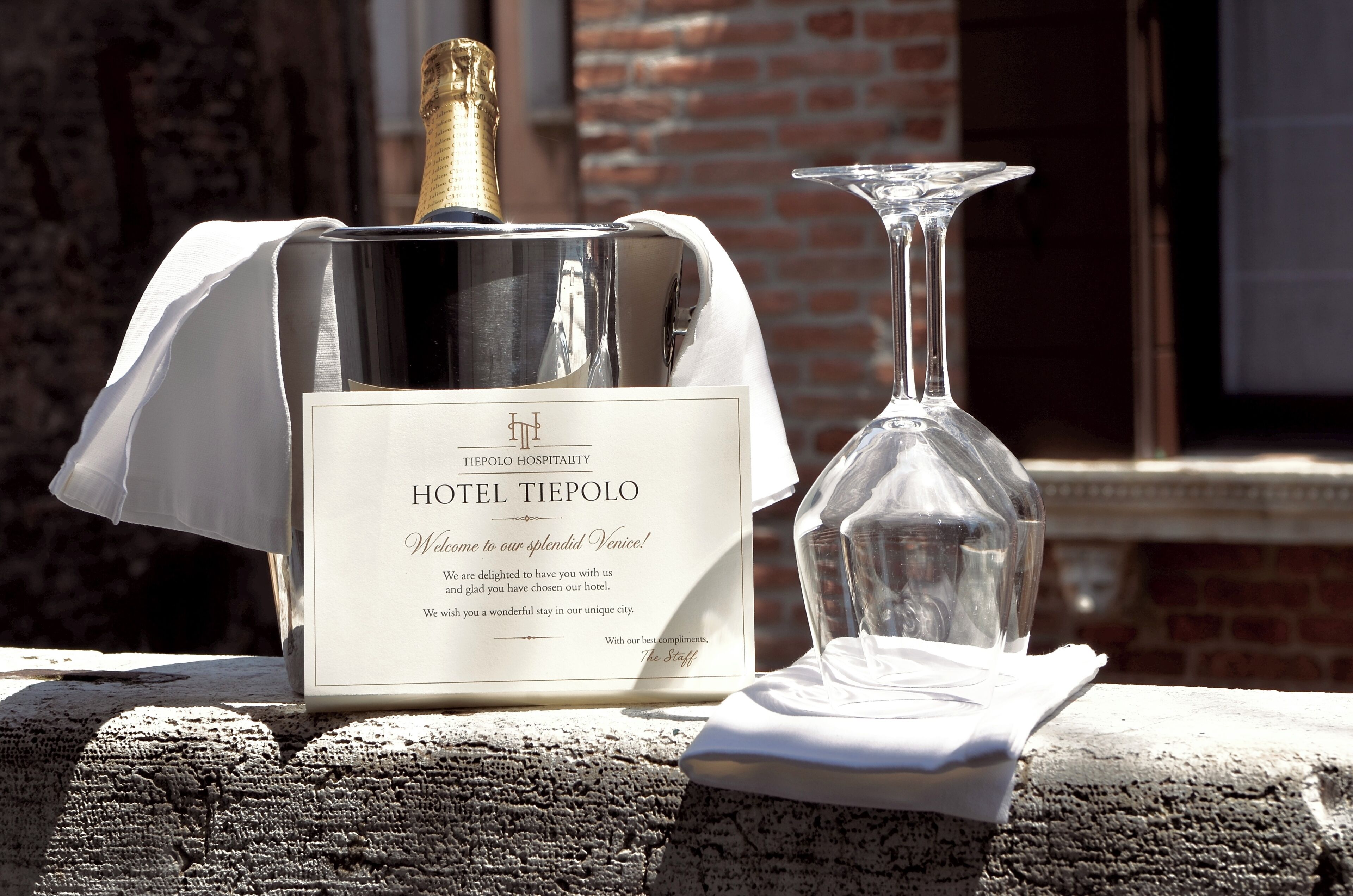 A bottle of Hotel Tiepolo wine and a glass on a table with a white cloth.