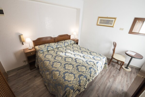 Un dormitorio con cama de madera, dos mesitas de noche con lámparas, una silla, una mesita redonda pequeña y un cuadro en la pared.