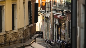 Une rue étroite bordée de bâtiments des deux côtés, avec des balcons et des espaces aménagés pour s’asseoir à l’extérieur.