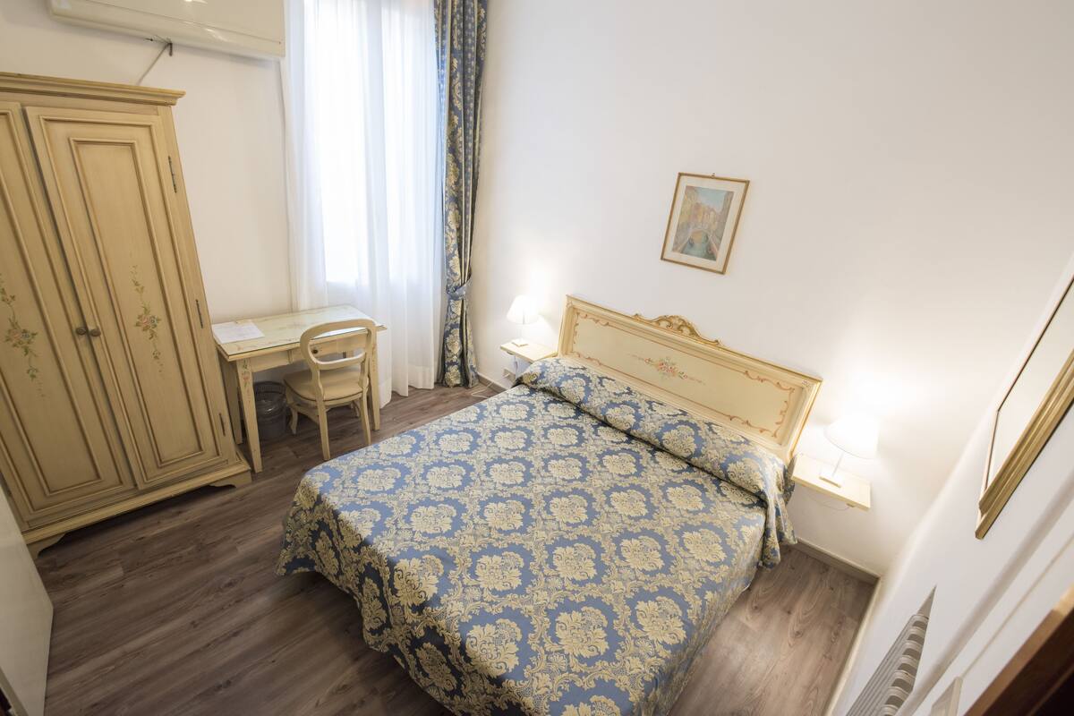 A bedroom with a bed, a desk, and a wardrobe.