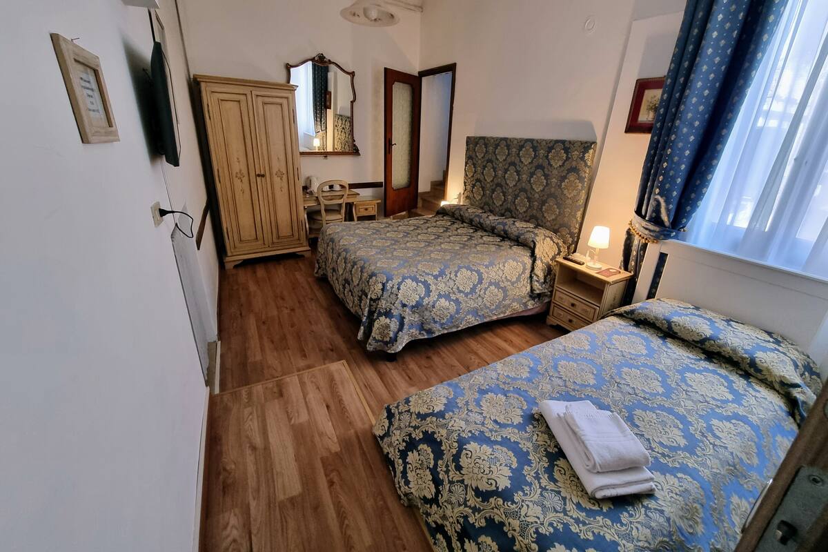 A bedroom with two beds, a wooden wardrobe, a desk, and a mirror.