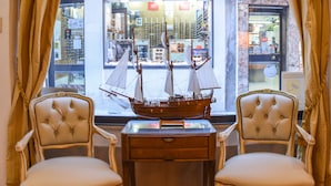 Une pièce comprenant deux fauteuils rembourrés, un bureau en bois et un modèle de bateau posé sur le bureau.