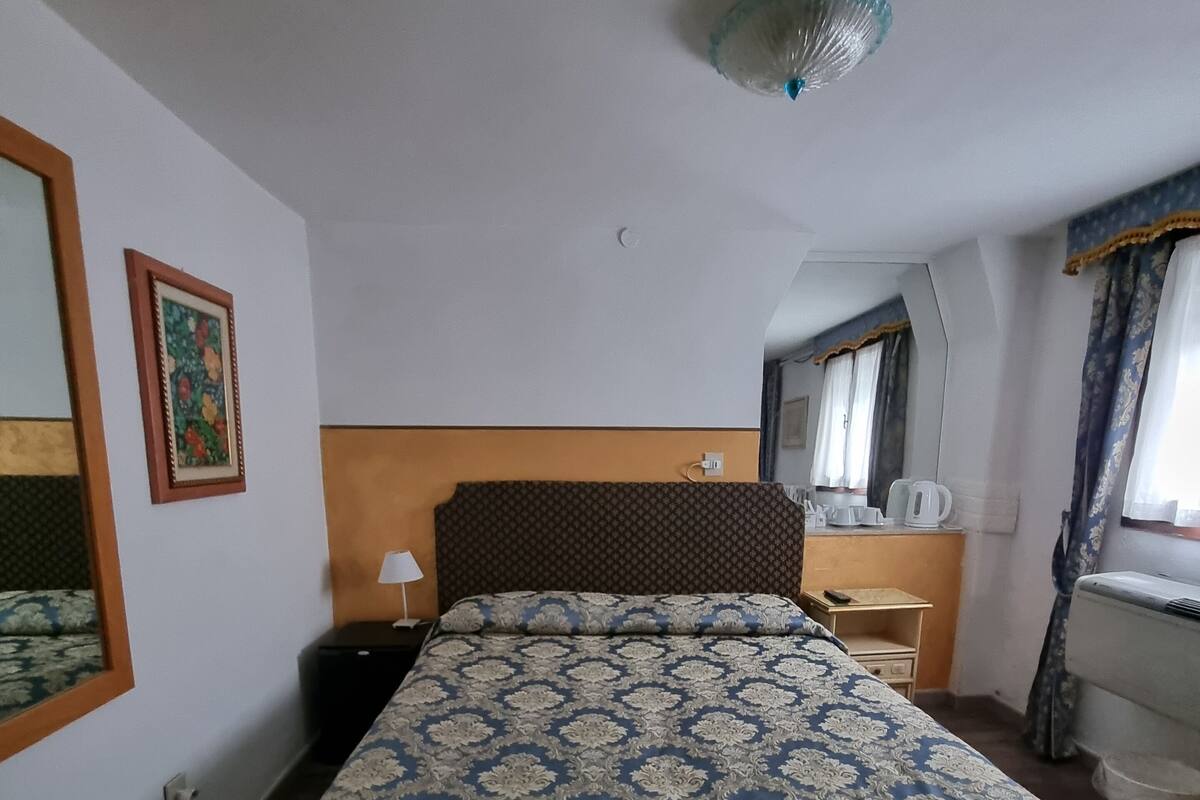 A bedroom with a bed, bedside table, lamp, and a mirror.