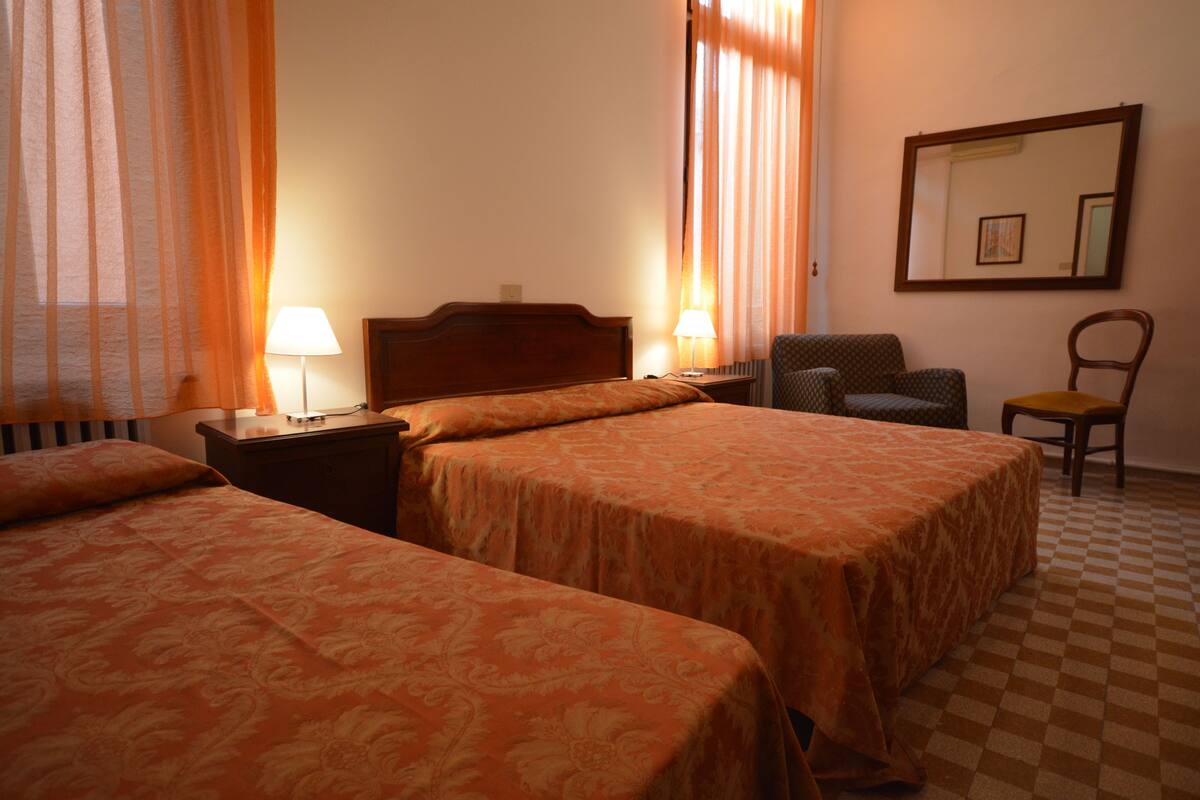 A hotel room with two beds, a chair, a nightstand with lamps, and a checkered floor.
