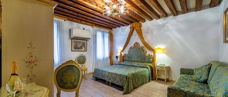 A bedroom with a four-poster bed, a sofa, a table with a bottle and glasses, and a chair.