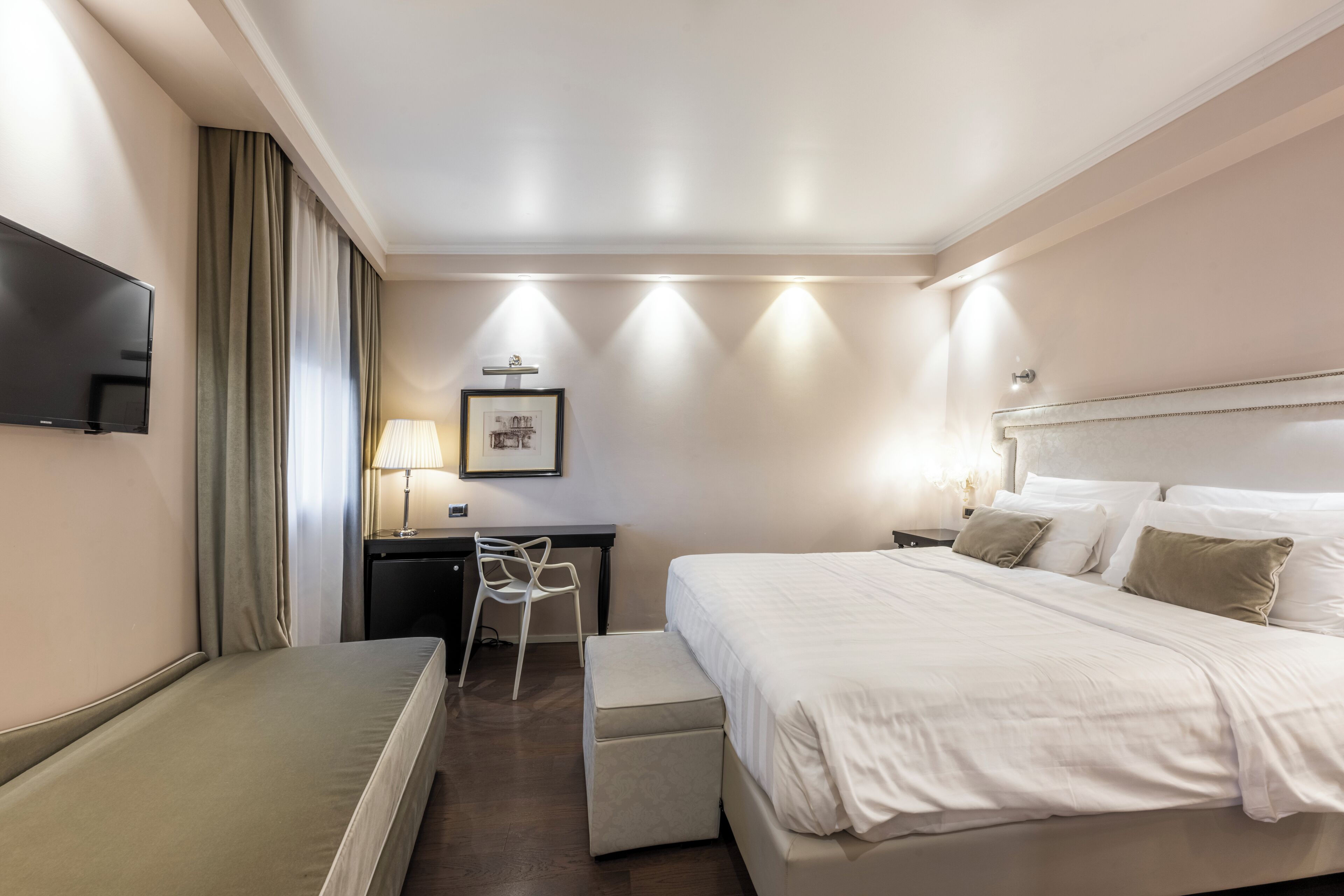 Quarto de hotel com cama, escrivaninha, cadeira, televisão e abajur.