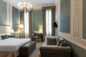 Camera d'albergo con un letto grande, un divano, una scrivania con una sedia, una TV e un lampadario.