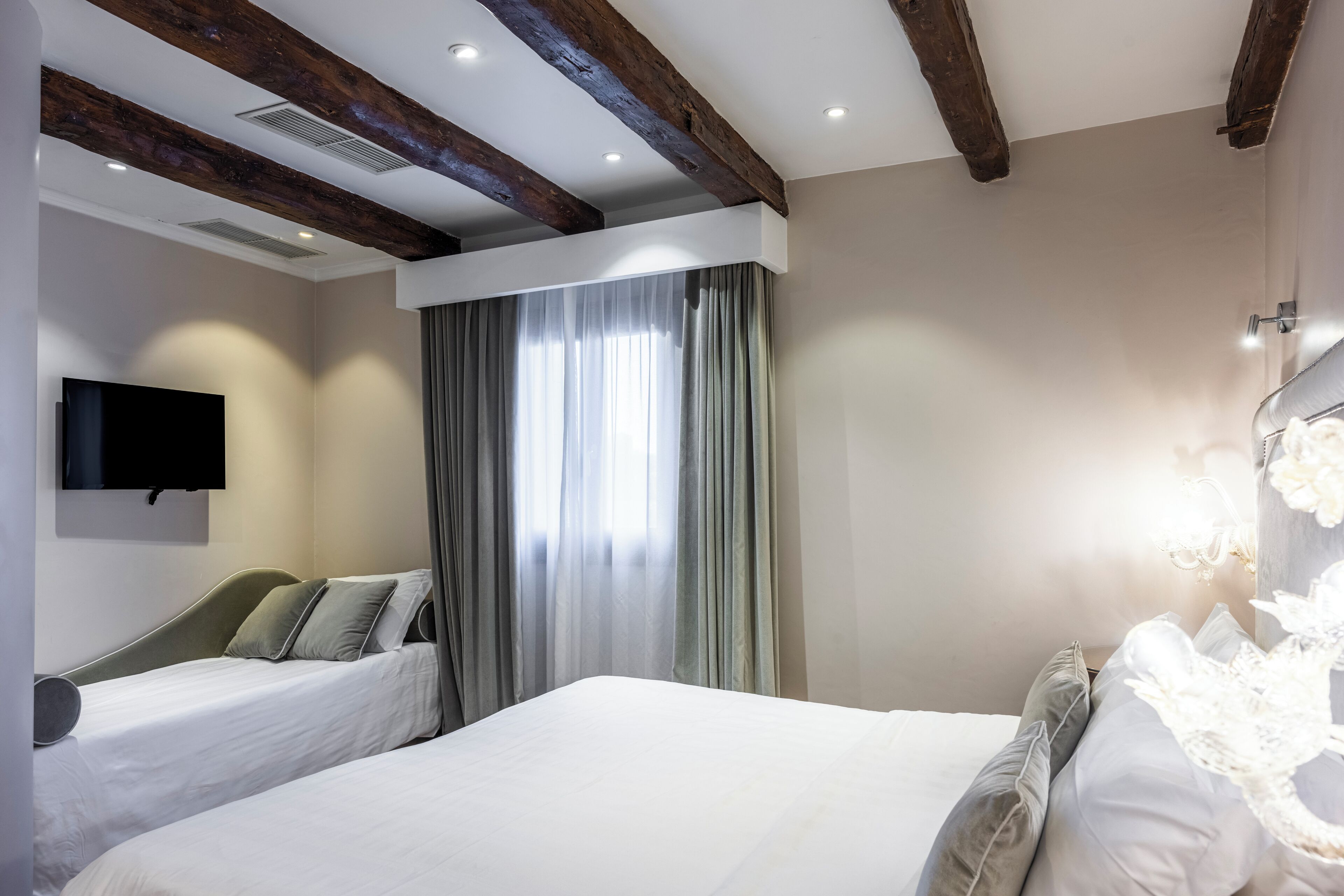 A hotel room with two beds, a flat-screen TV mounted on the wall, and a large window with curtains.