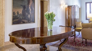 Une grande pièce avec une vaste table en bois, un lustre, un tableau au mur et un vase rempli de fleurs.