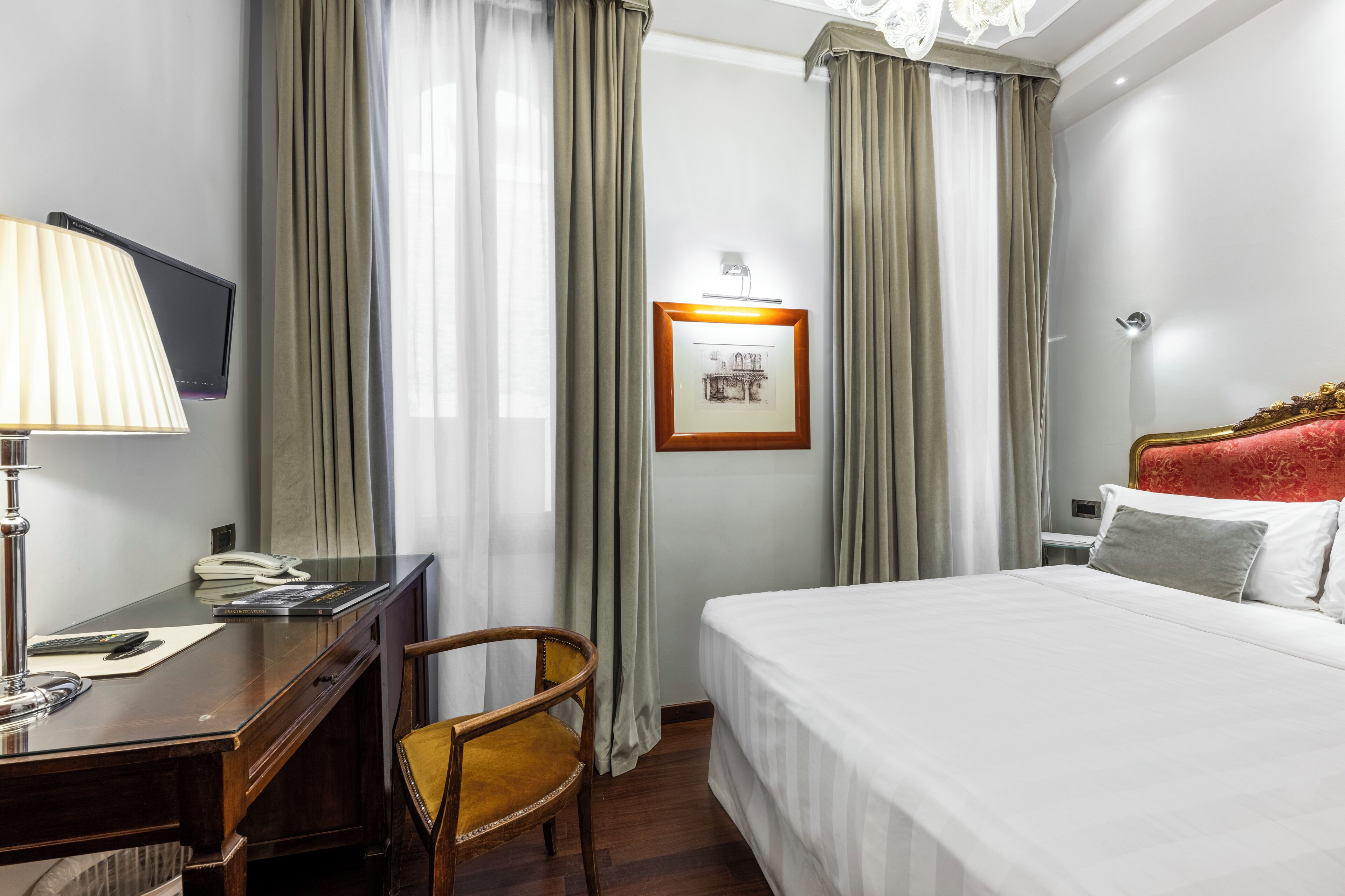 A hotel room with a bed, a desk with a lamp, a chair, a TV, and curtains.