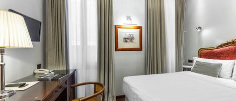 A hotel room with a bed, a desk with a lamp, a chair, a TV, and curtains.