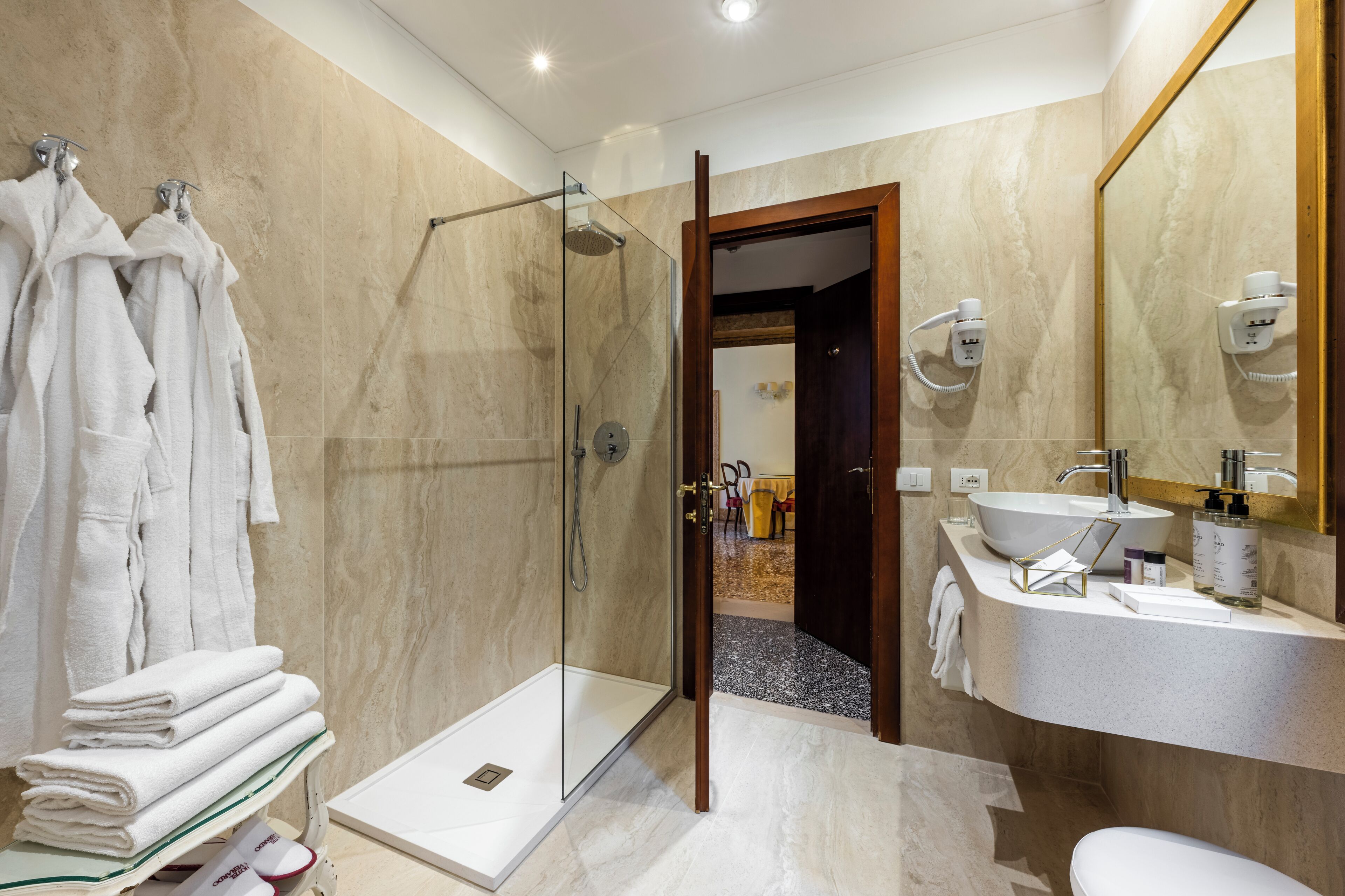 A modern bathroom with a glass shower enclosure, a vanity with a sink and mirror, and a stack of white towels.