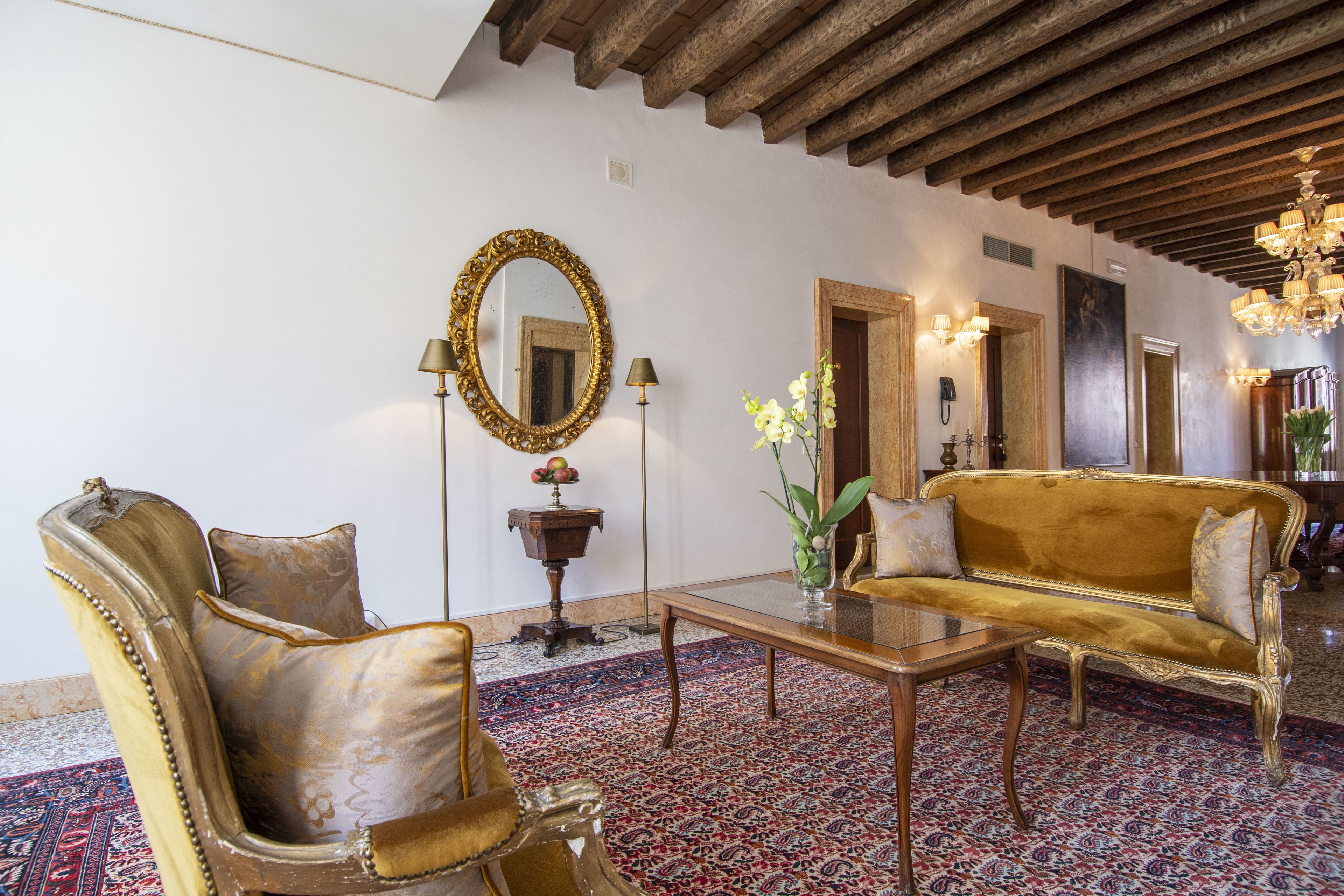 A room with a large ornate mirror, a golden sofa, a wooden coffee table, and a patterned carpet.