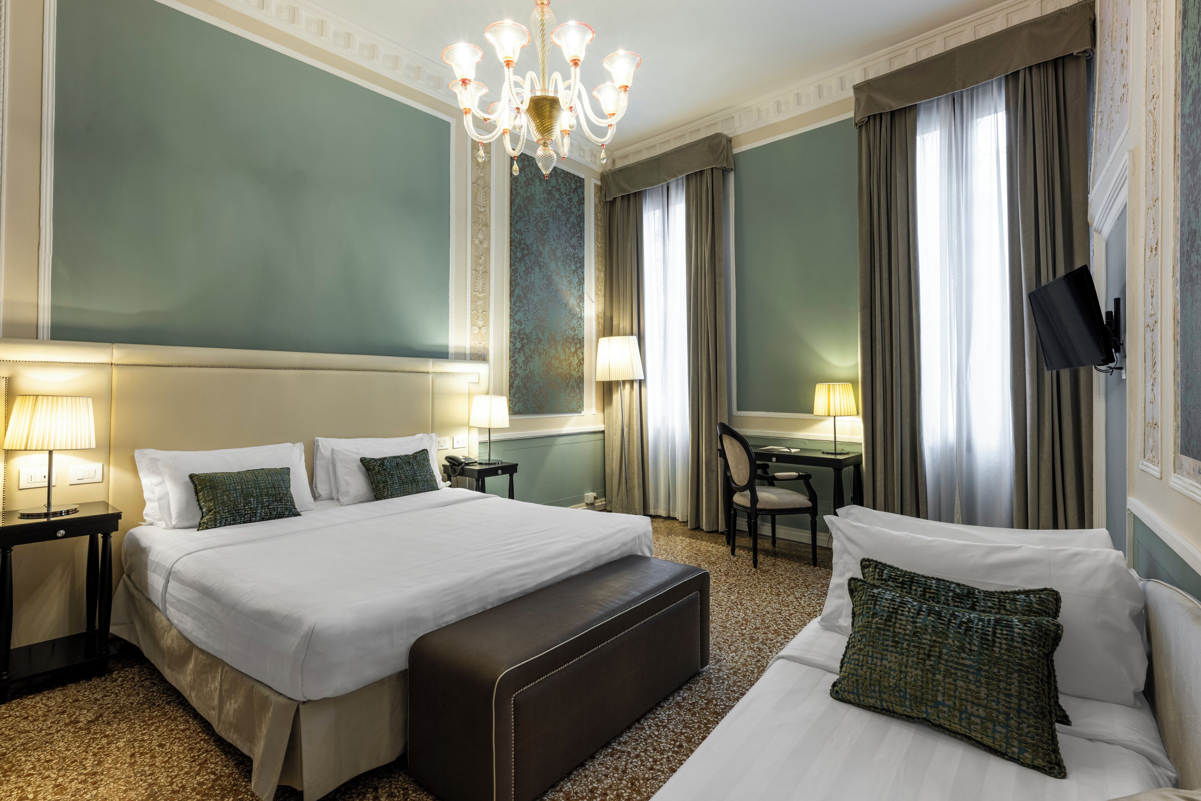 A hotel room with a large bed, a desk, a chair, and a television.