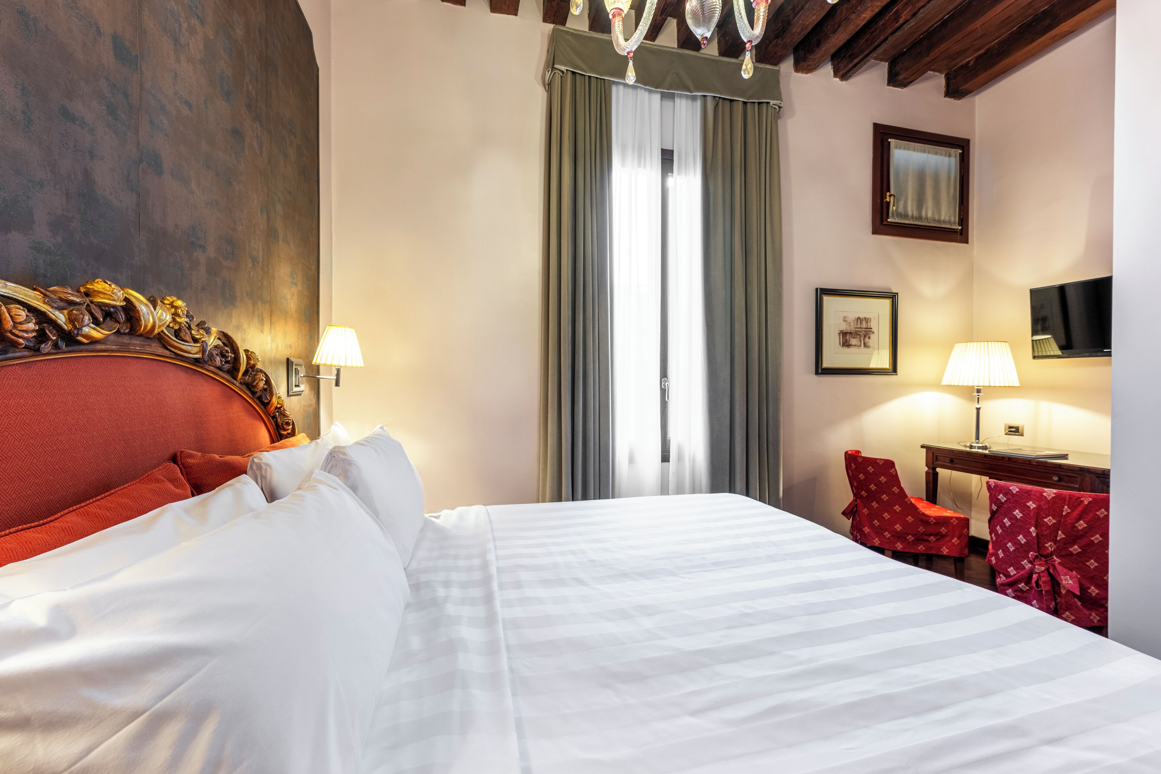 Une chambre d’hôtel avec un grand lit, un bureau avec une chaise, une télévision et une fenêtre avec des rideaux.