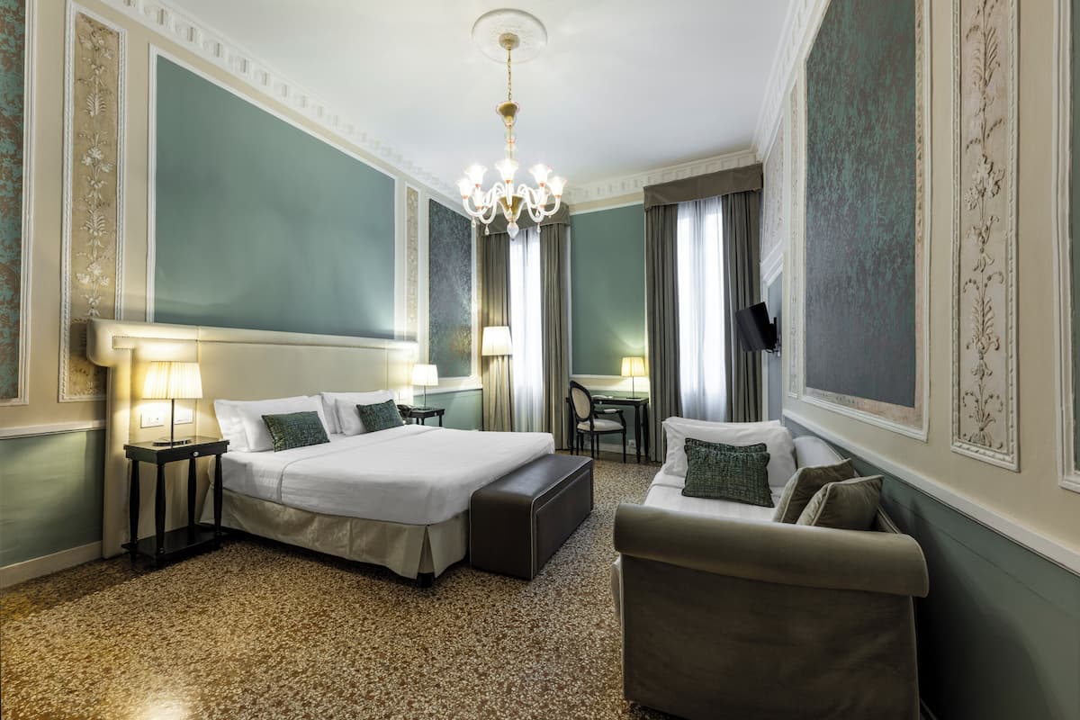 A hotel room with two beds, a sofa, a desk, and a chandelier.