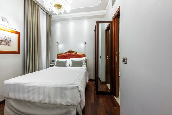 Un dormitorio ordenado con una cama grande, una araña de cristal, un cuadro en la pared y un espejo en la habitación contigua.
