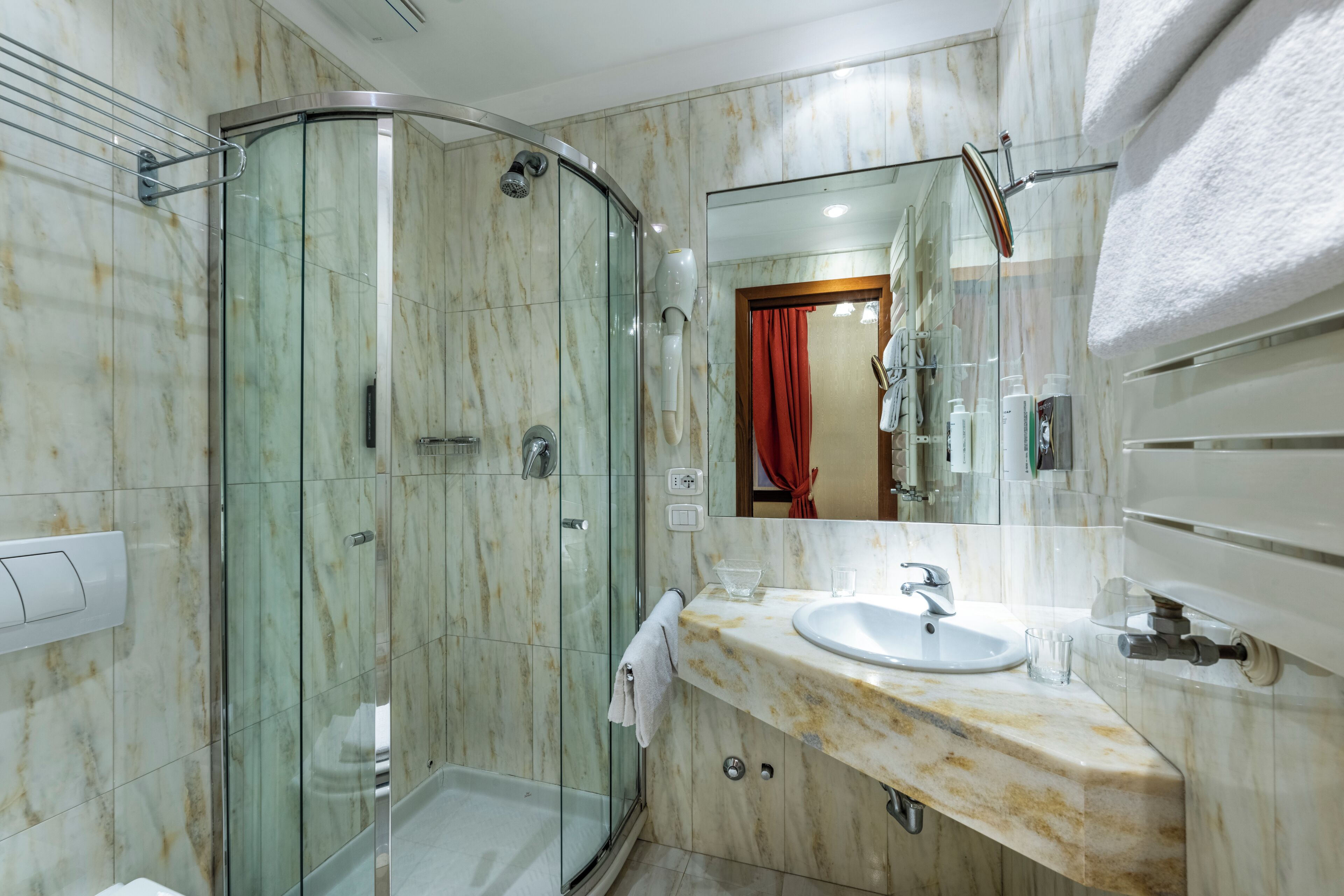 A modern bathroom with a glass-enclosed shower, a marble vanity, and a large mirror.