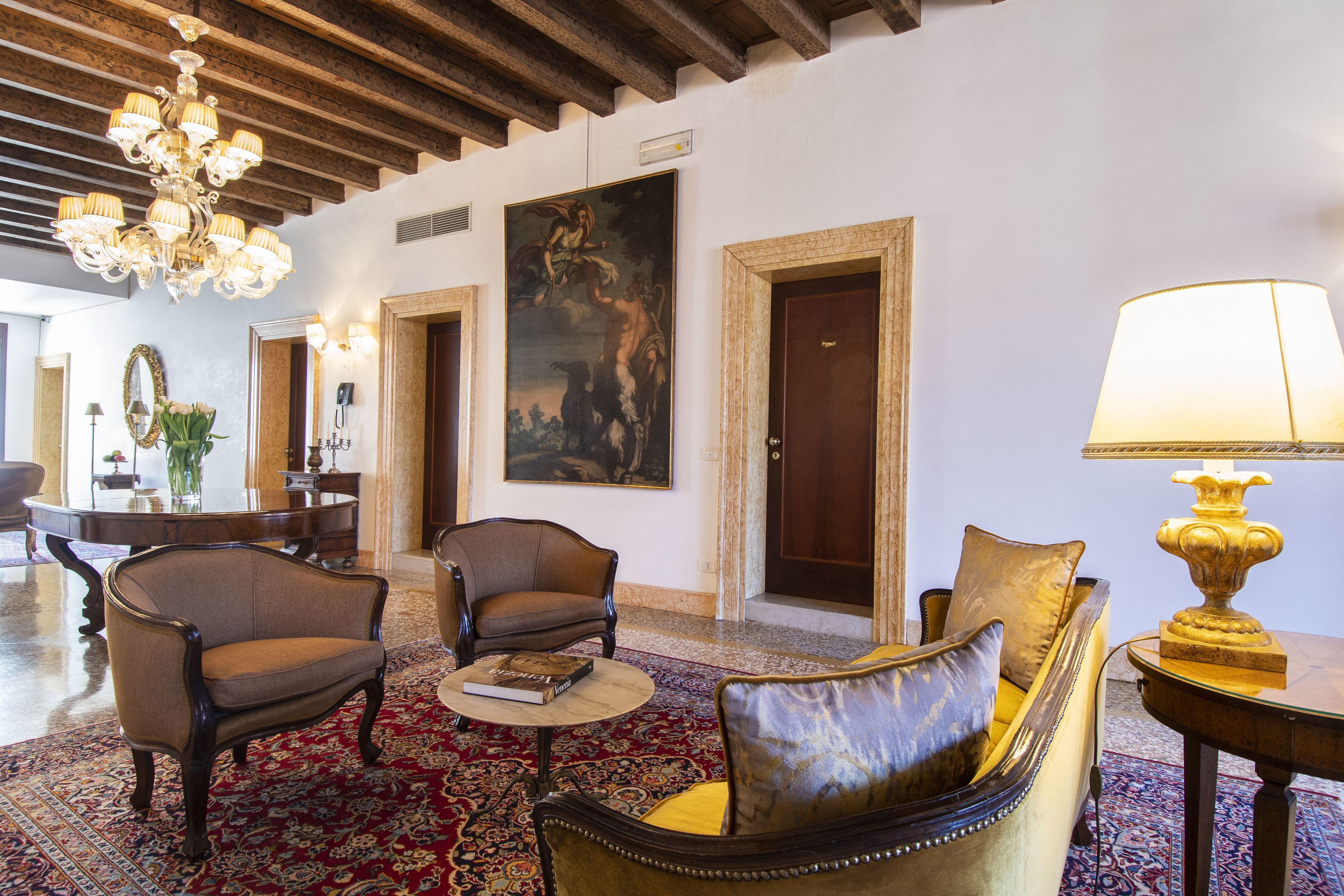 A lobby with a chandelier, a painting, and a sofa with a lamp.