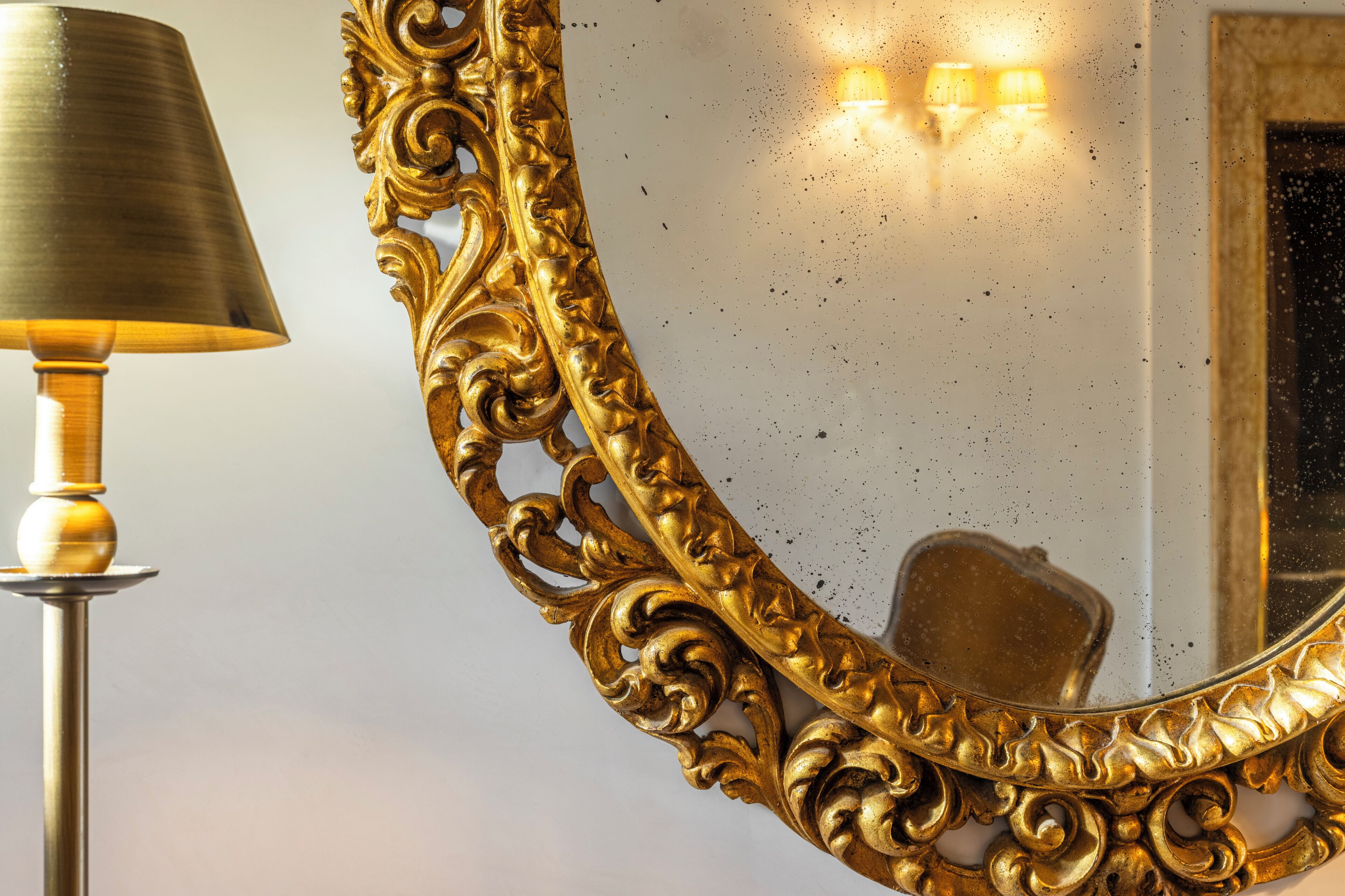 Ein goldverzerrter Spiegel mit einer Lampe daneben.