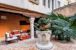Un patio con una mesa de piedra, un sofá con cojines rojos y una planta en maceta.
