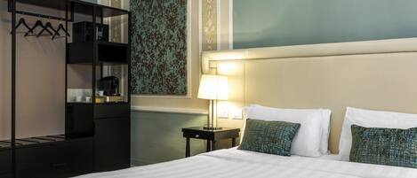 Habitación de hotel con cama, mesita de noche con lámpara, armario y pared con papel tapiz estampado.