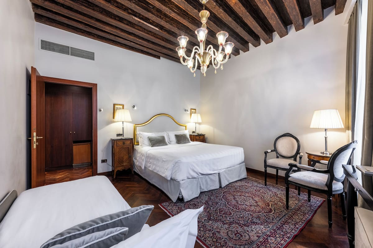 A bedroom with a bed, bedside tables, a chair, a chandelier, and a patterned rug.