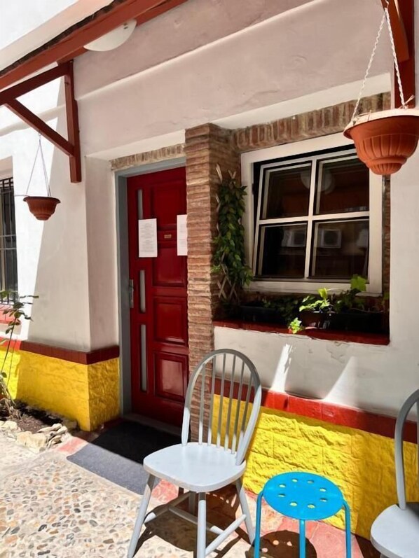 A building with a red door, a window with plants, and two chairs outside.