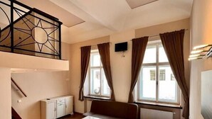 A compact room with a bed, a sofa, a small table, and a staircase leading to an upper level. - Residence Casa Italia  (Prague)