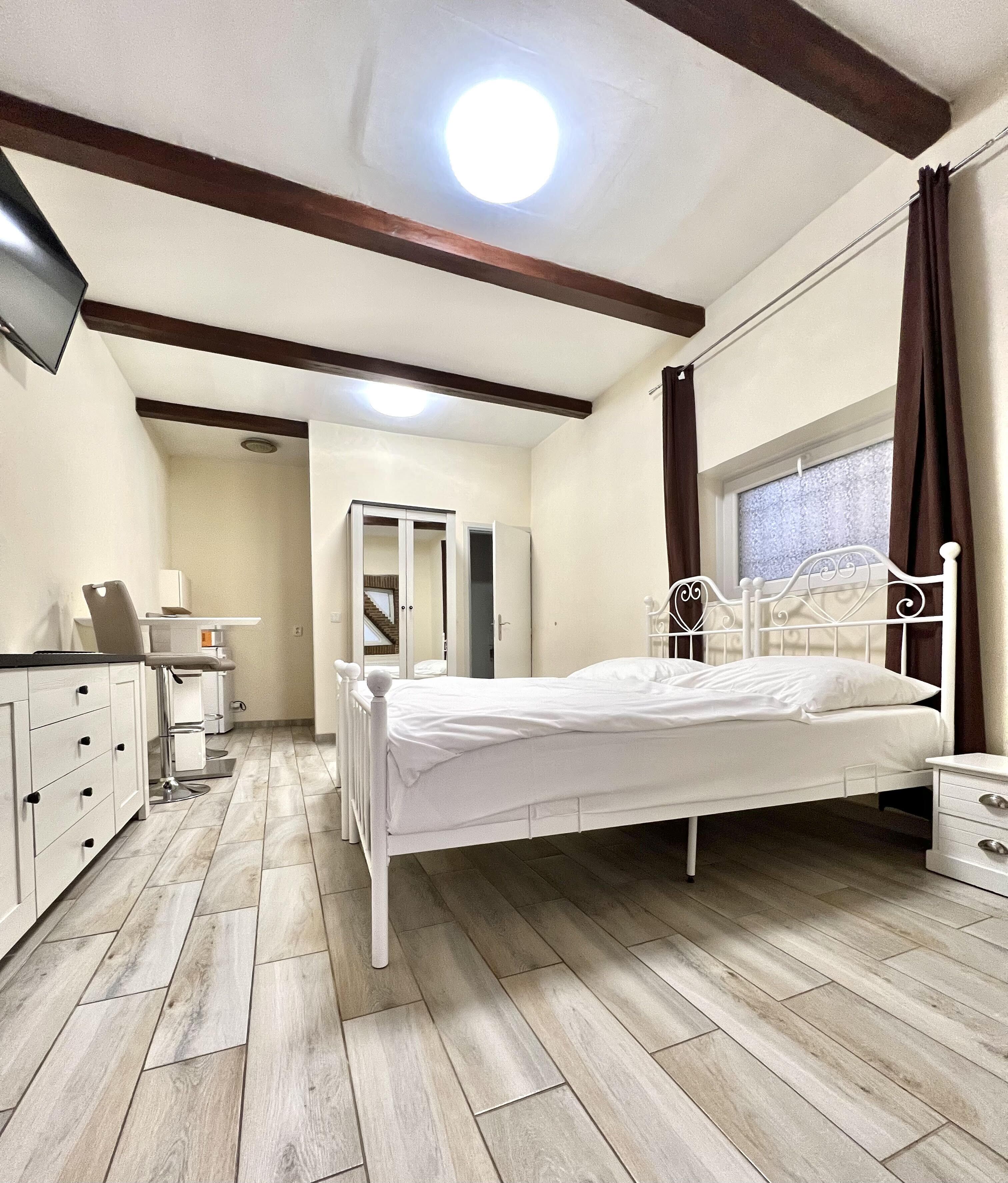 Un dormitorio con cama, mesitas de noche, armario, espejo y ventana con cortinas.
