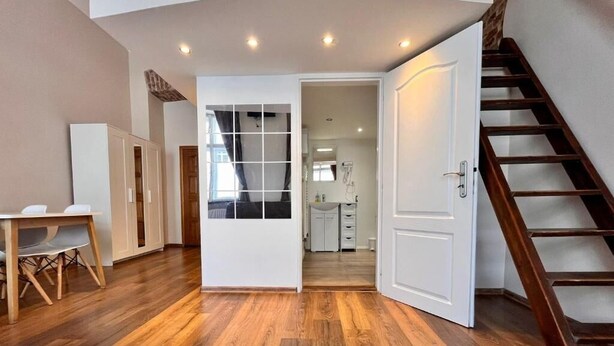 A spacious room with wooden flooring, a dining area with a table and chairs, a staircase, and a view into a kitchen area. - Residence Casa Italia  (Prague)