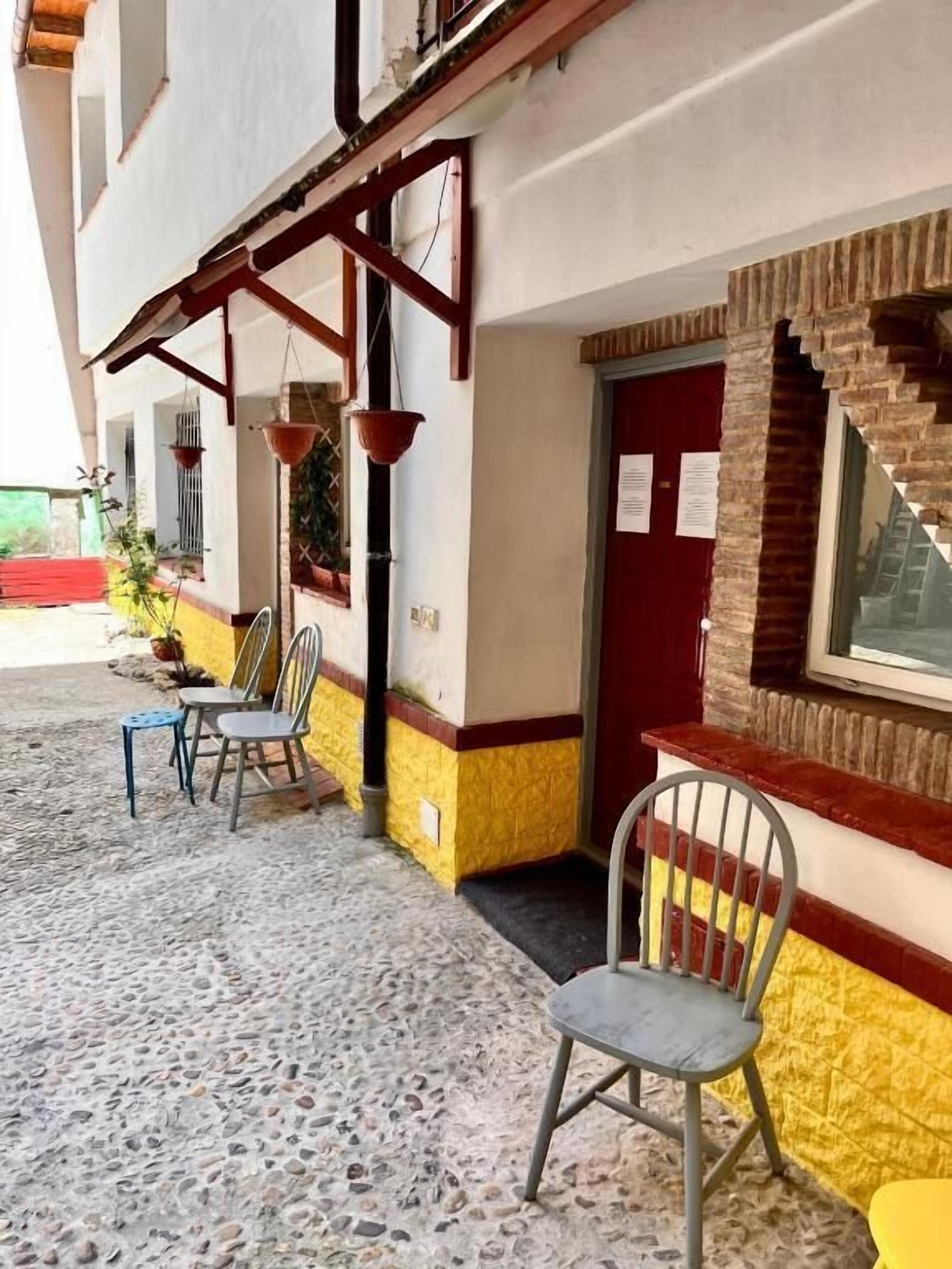 Ein Gebäude mit einer gefliesten Terrasse, Sitzgelegenheiten im Freien und einer roten Tür.