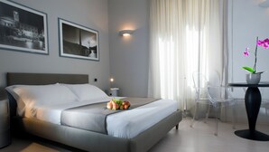 A modern hotel room with a bed, a bedside table with a lamp, a chair, and a small table with a potted orchid. - Best Vatican B&B (Rome)