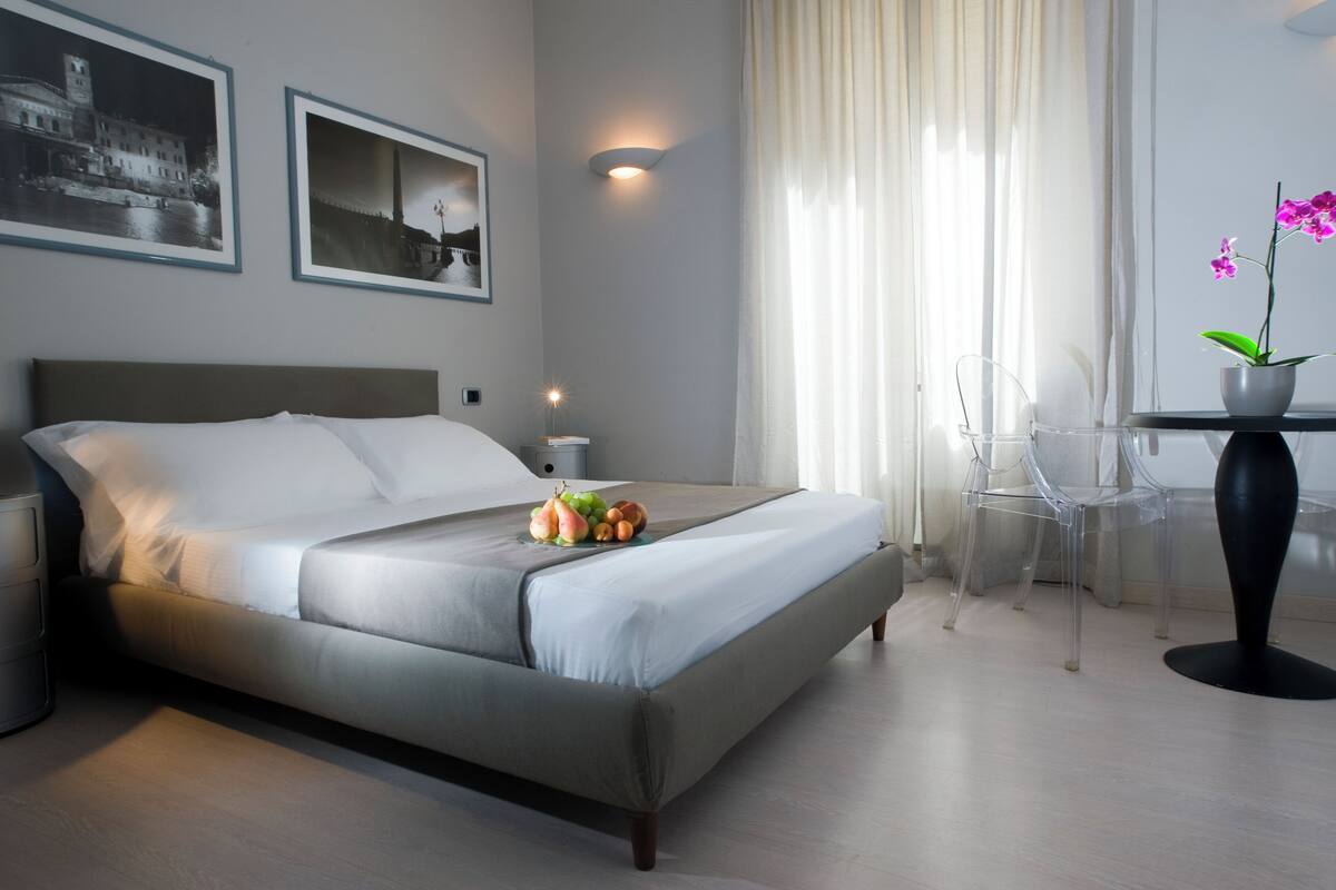 A modern hotel room with a bed, a bedside table with a lamp, a chair, and a small table with a potted orchid.