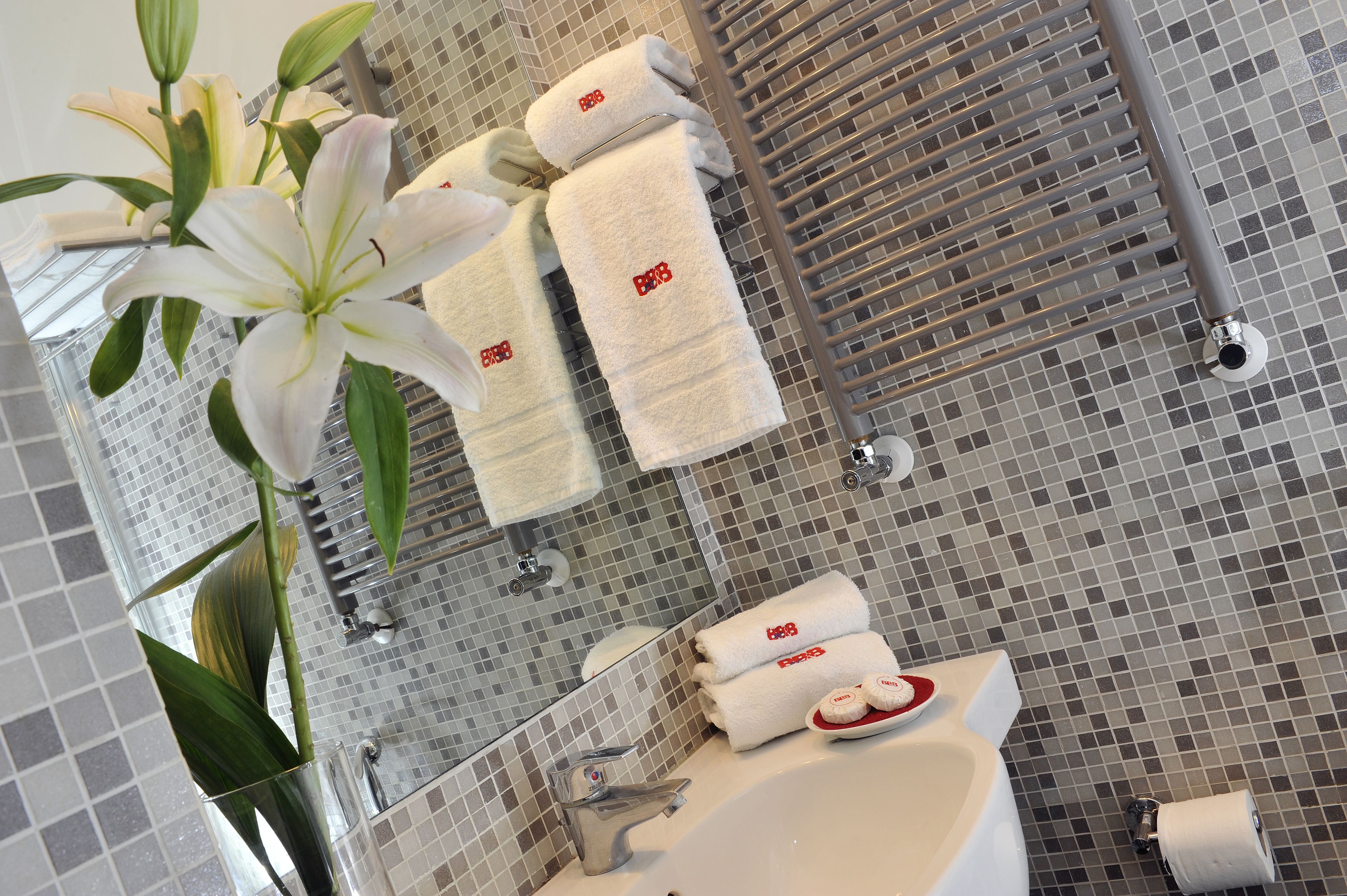 A bathroom with a tiled floor, a sink, a mirror, and towels with a logo.