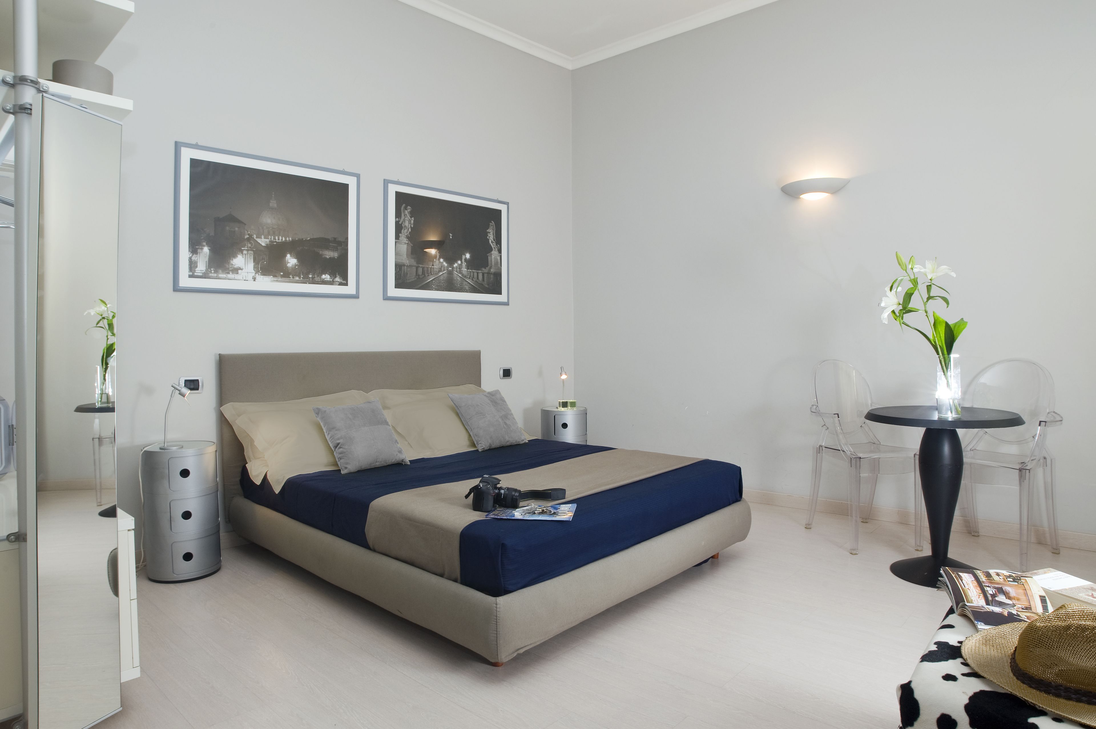 Un dormitorio moderno con cama, mesitas de noche, una pequeña mesa con un florero y dos cuadros en la pared.