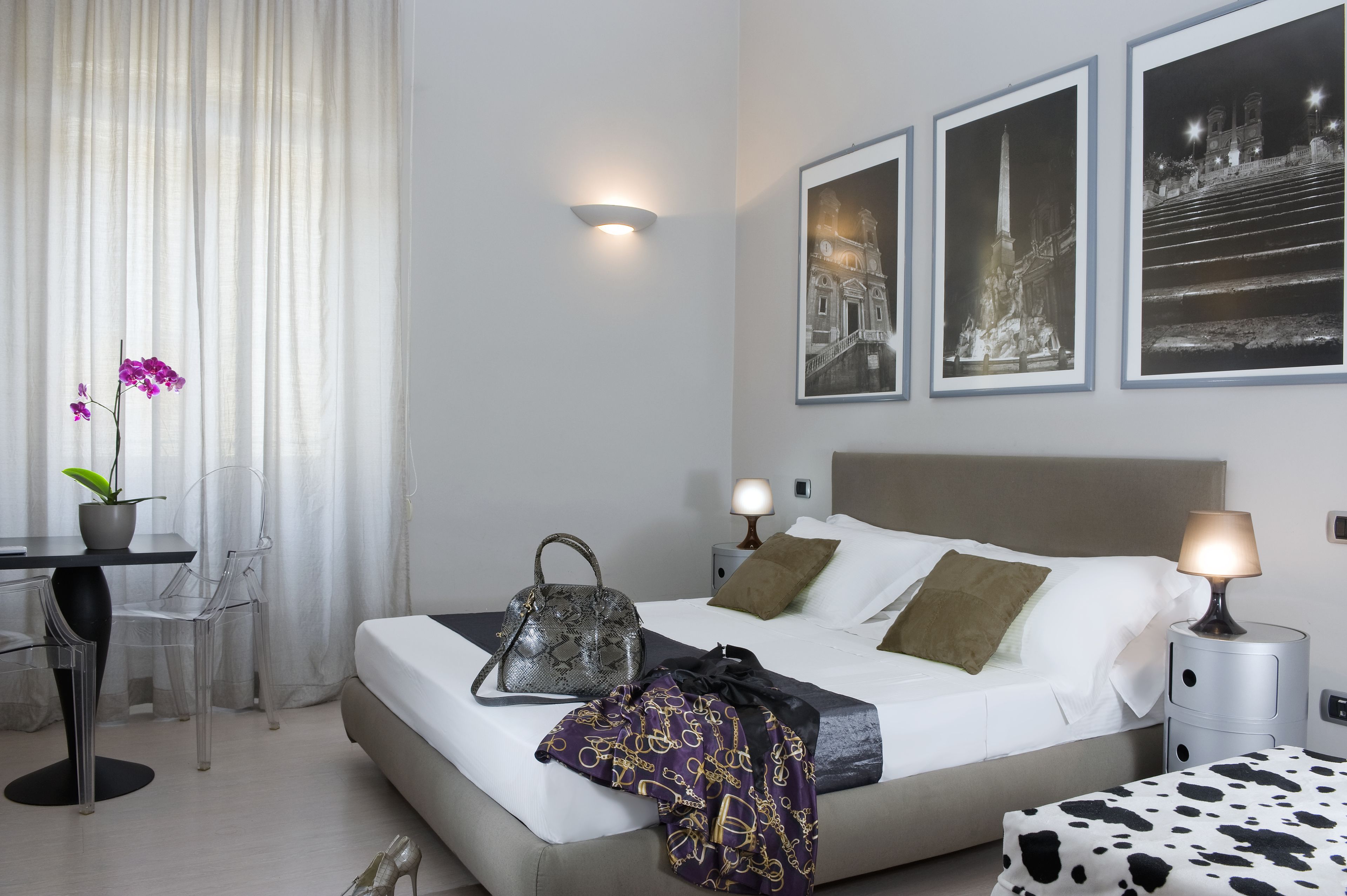 A modern hotel room with a bed, bedside tables, a desk, and chairs.