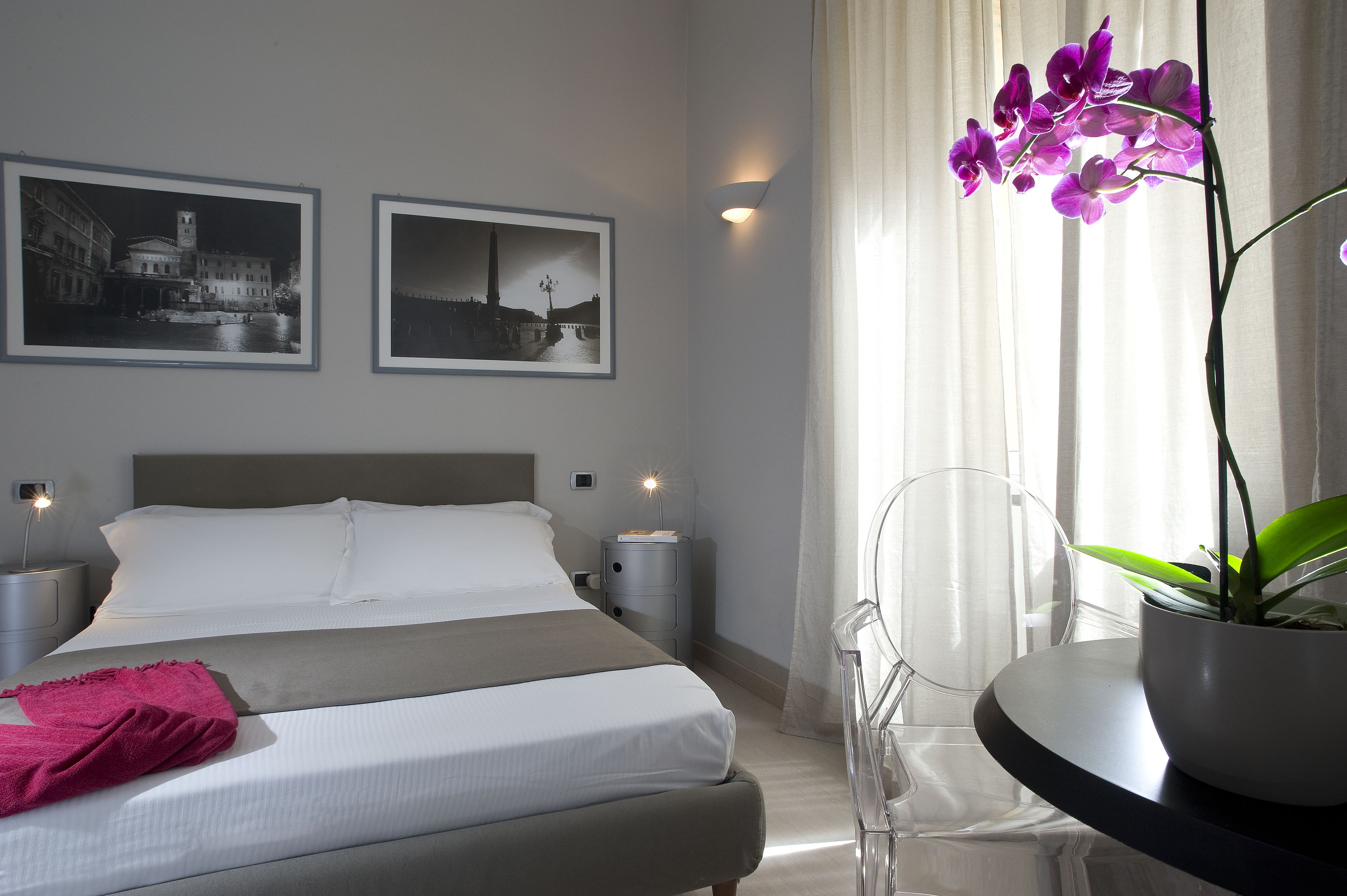 A hotel room with a bed, nightstands, a potted orchid, and two framed photographs on the wall.