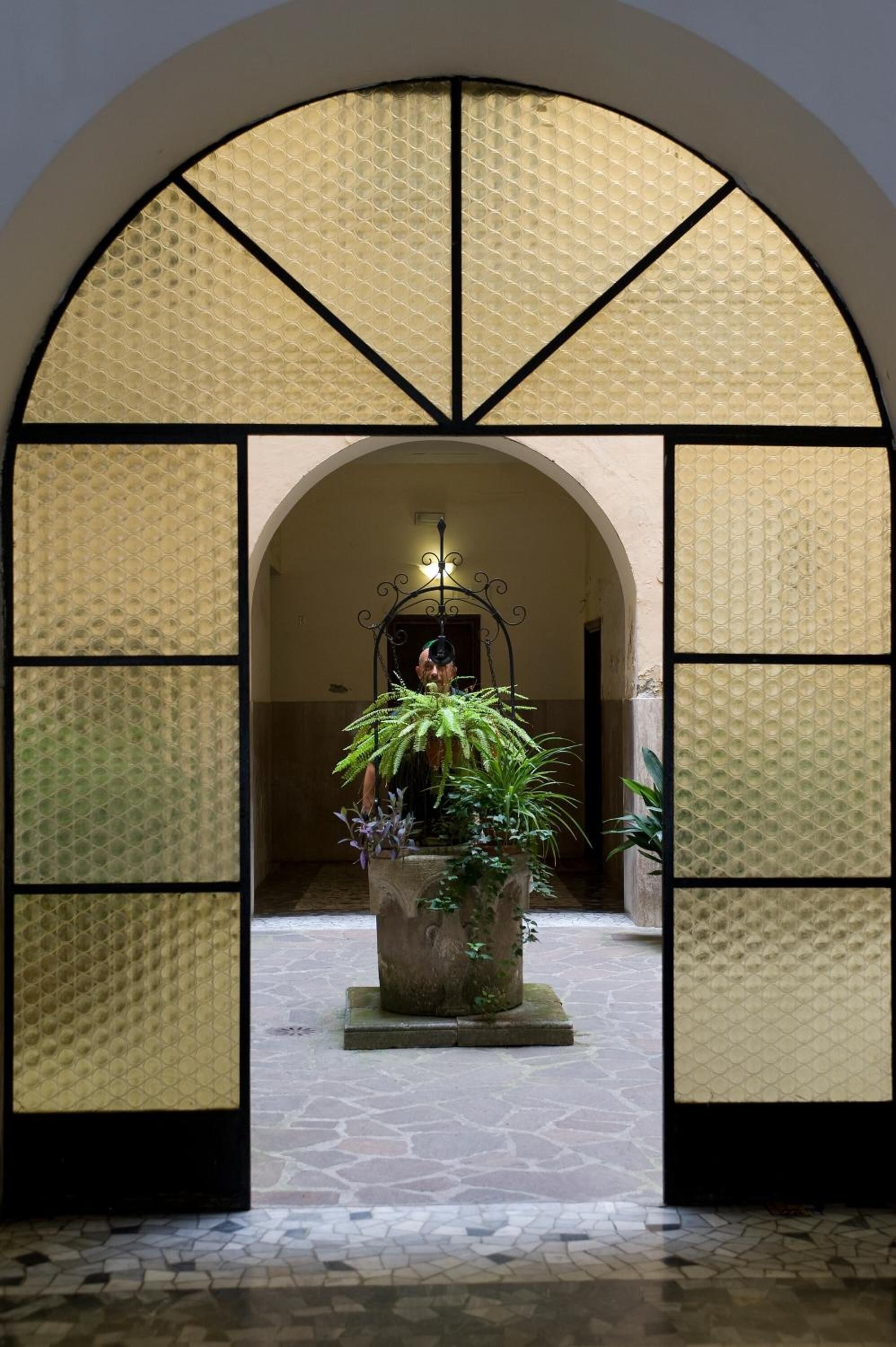 Un portail en arc surmonté d’un sol carrelé, qui mène à une pièce agrémentée d’un lustre et de plantes en pot.