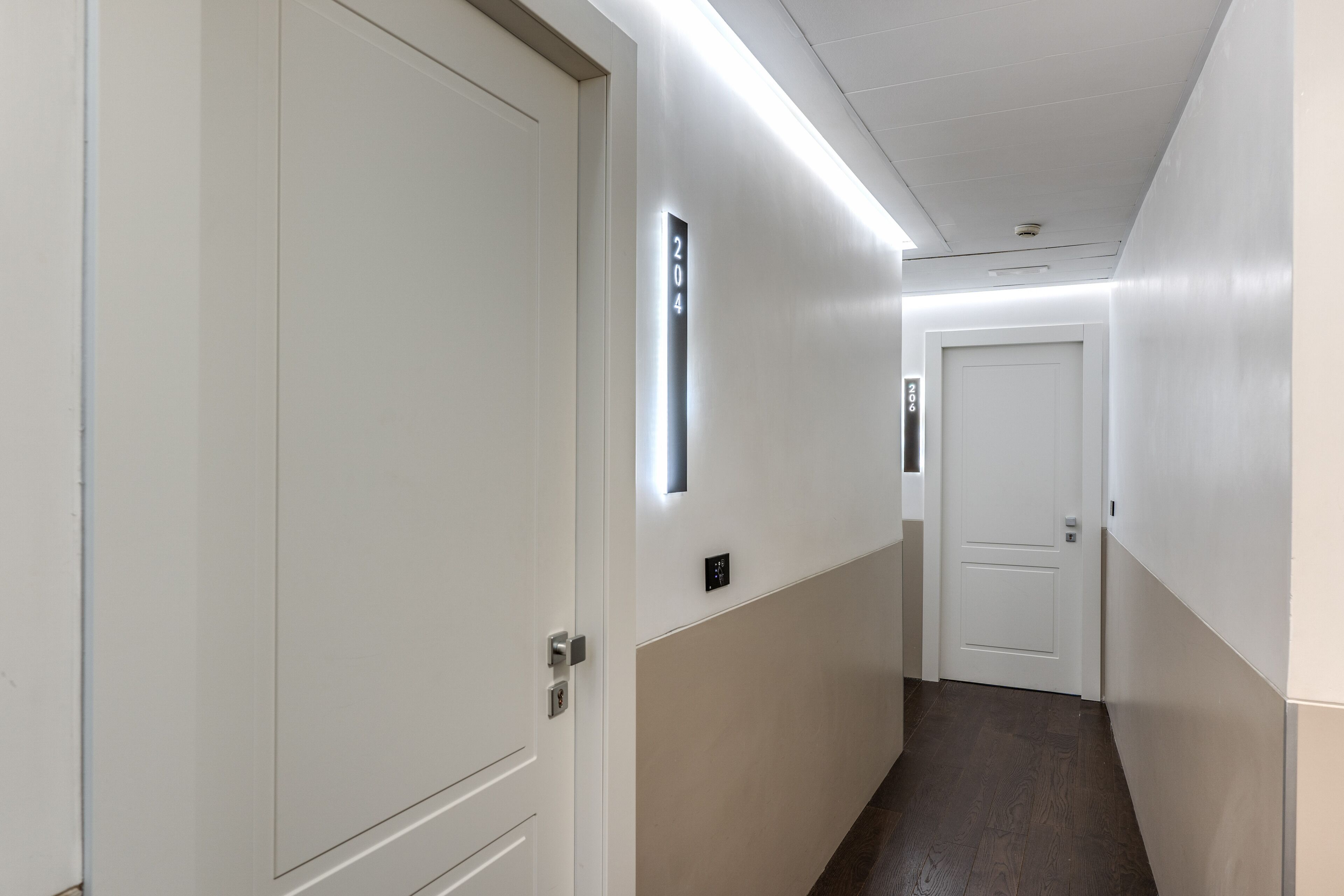 A hallway with a door labeled 204, a light switch, and a door at the end.