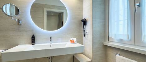 A modern bathroom with a large mirror, a built-in sink, a hairdryer, and a towel rack.