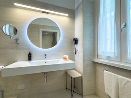 A modern bathroom with a large mirror, a built-in sink, a hairdryer, and a towel rack.