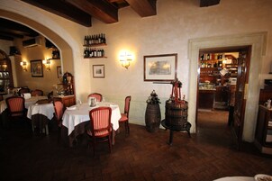 Et restaurantinteriør med træborde og stole, vinflasker på hylder og en murstensgulv.
